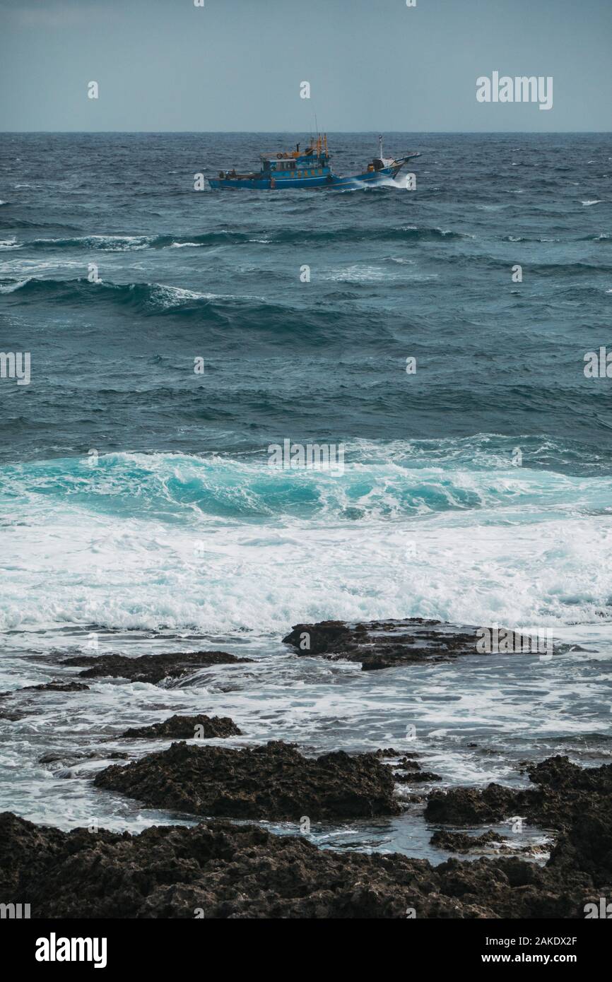 A small fishing boat sails across rough seas in front of Taiwan's southernmost point Stock Photo