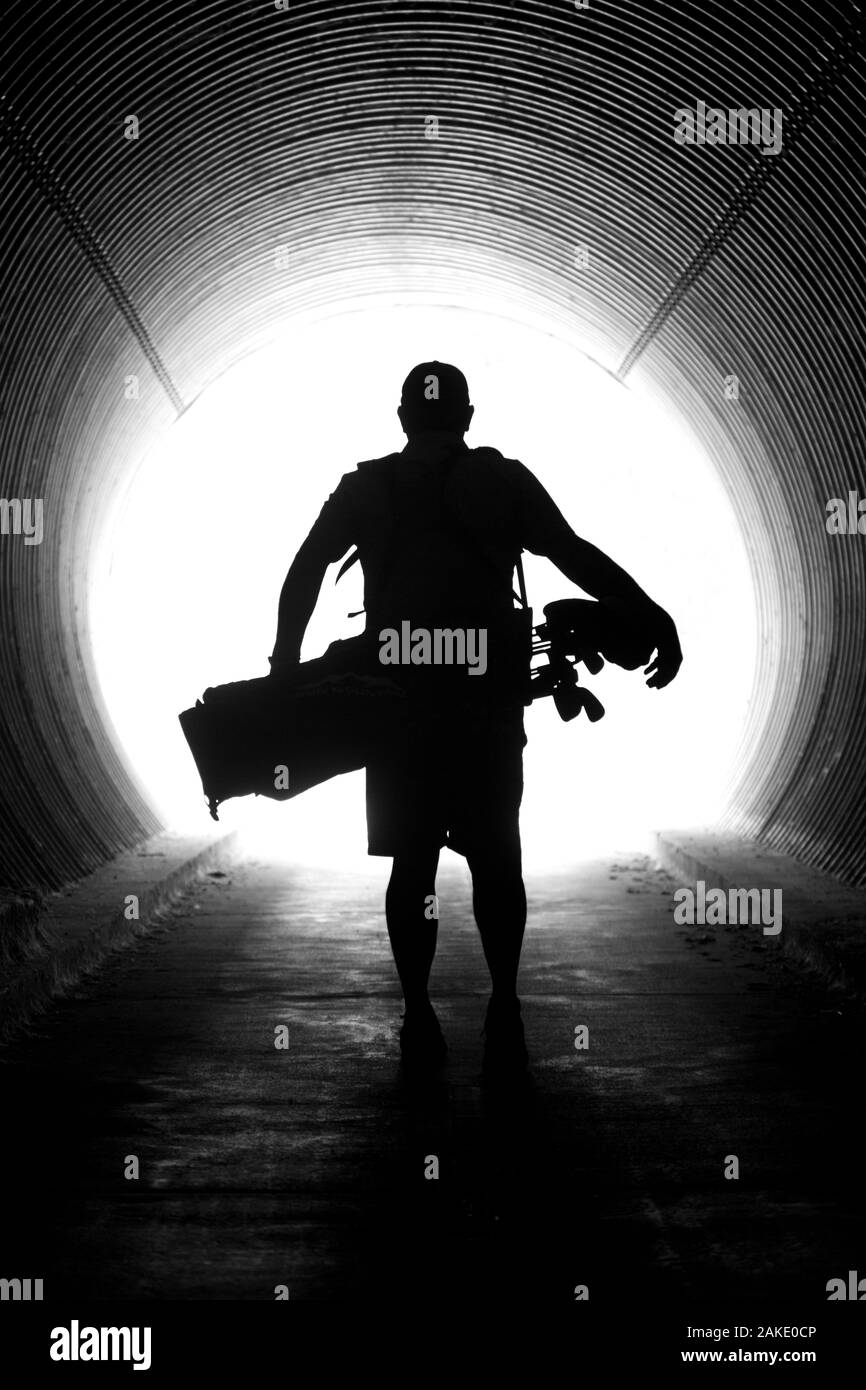 Silhouette of Golfer walking through tunnel with golf bag on shoulders Stock Photo