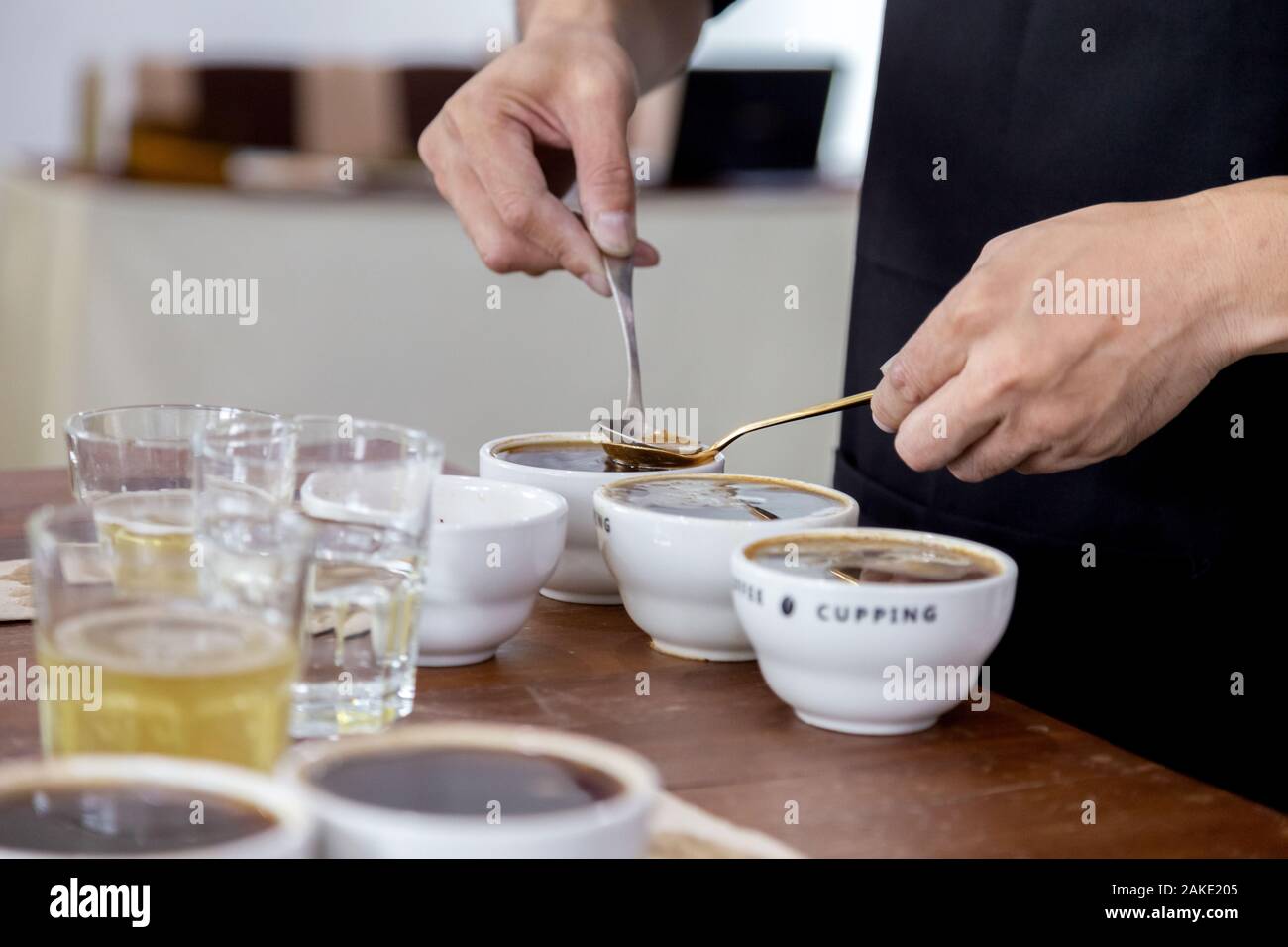 professional Q Grader preparing to test and inspecting the quality of coffee and skim off the coffee grounds from ceramic cup on the table. Stock Photo