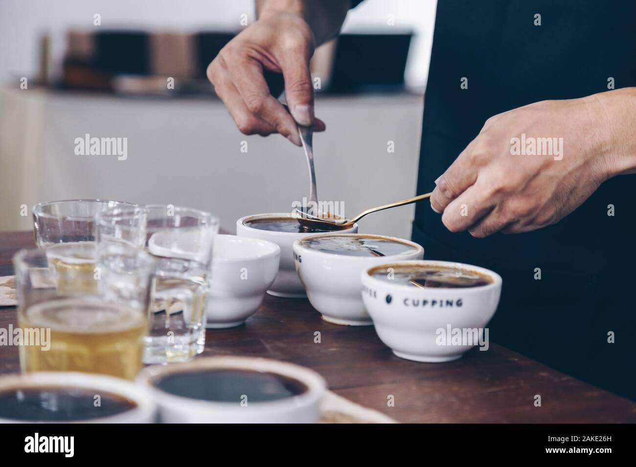 professional Q Grader preparing to test and inspecting the quality of coffee and skim off the coffee grounds from ceramic cup on the table. Stock Photo