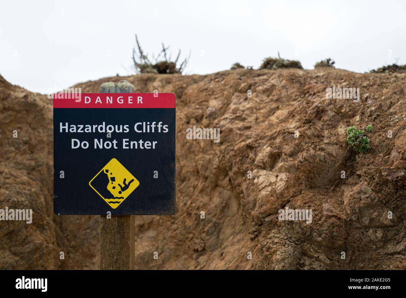 Danger hazardous cliffs do not enter with person falling sign leading up path hiking trail Stock Photo