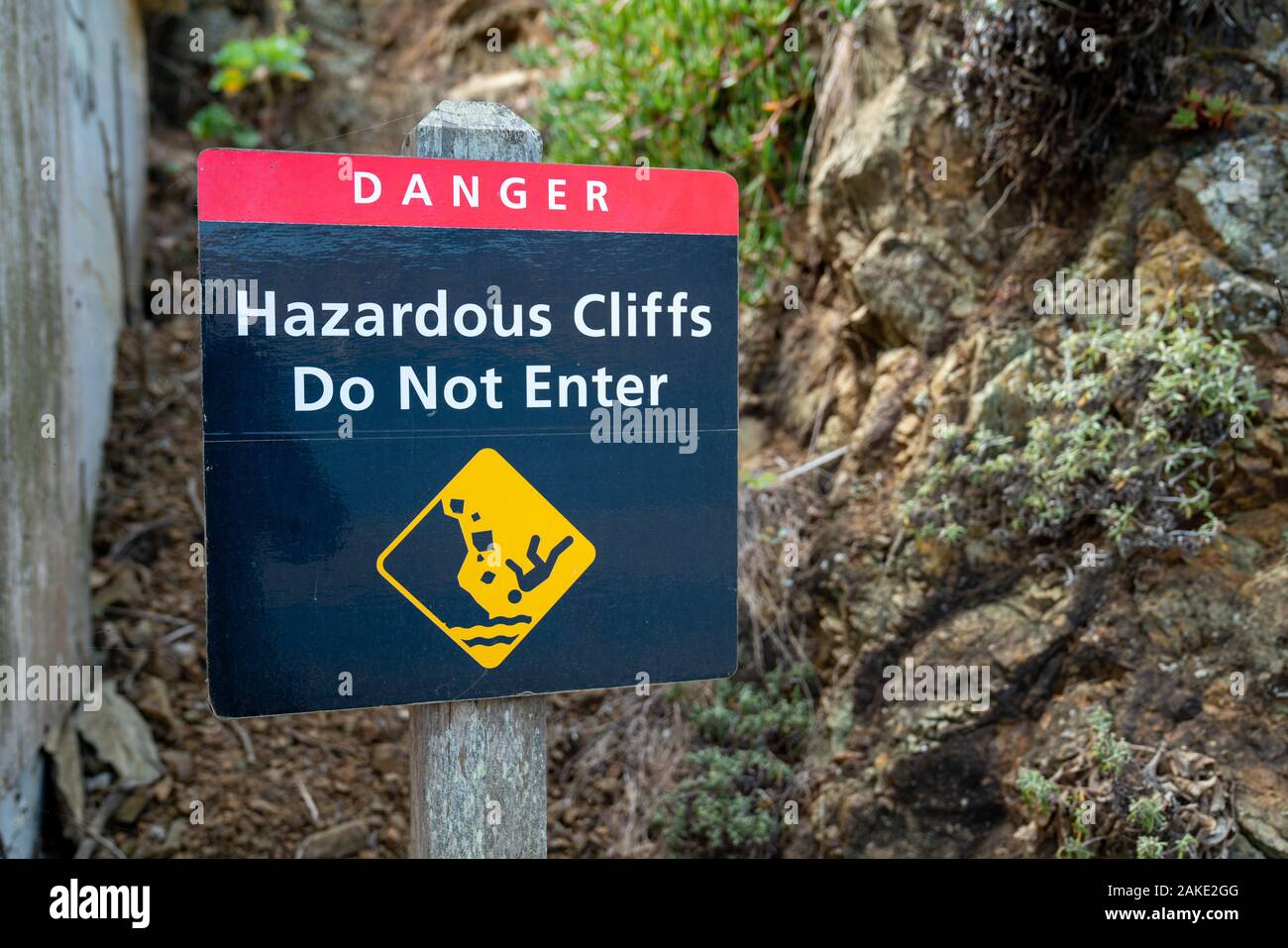 Danger hazardous cliffs do not enter with person falling sign on wooden post leading up hill Stock Photo