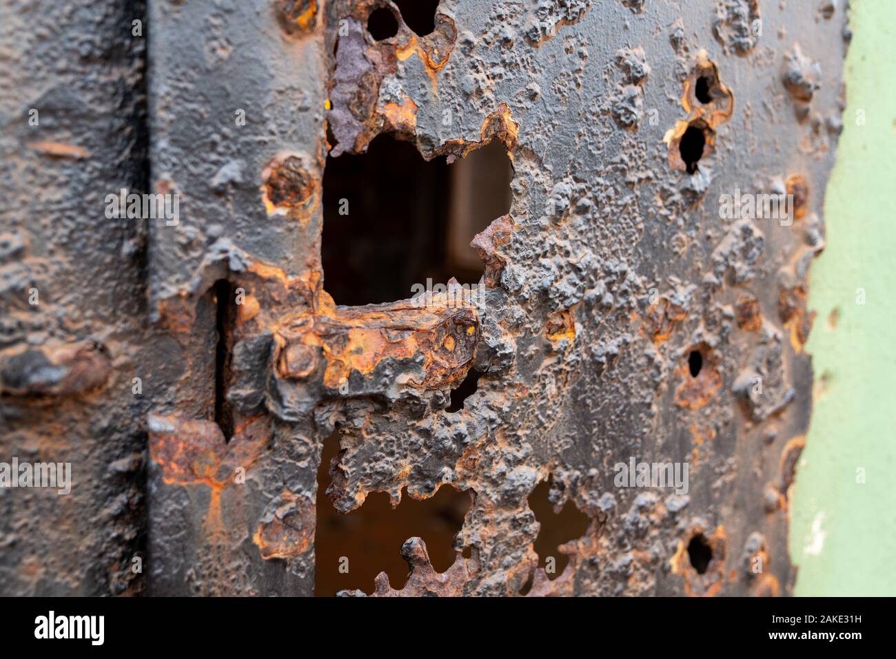 Steel door eroded by elements with holes into building Stock Photo