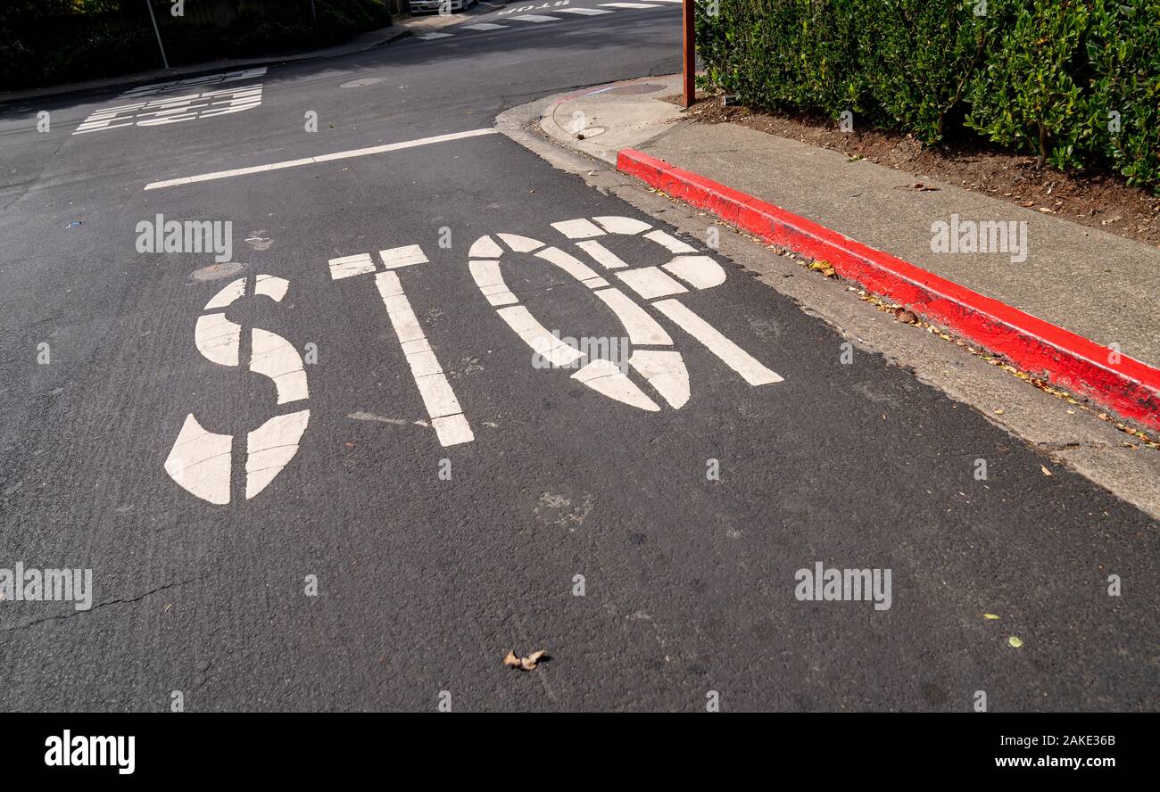 Stop sign painted on asphalt of red curb street at intersection Stock Photo