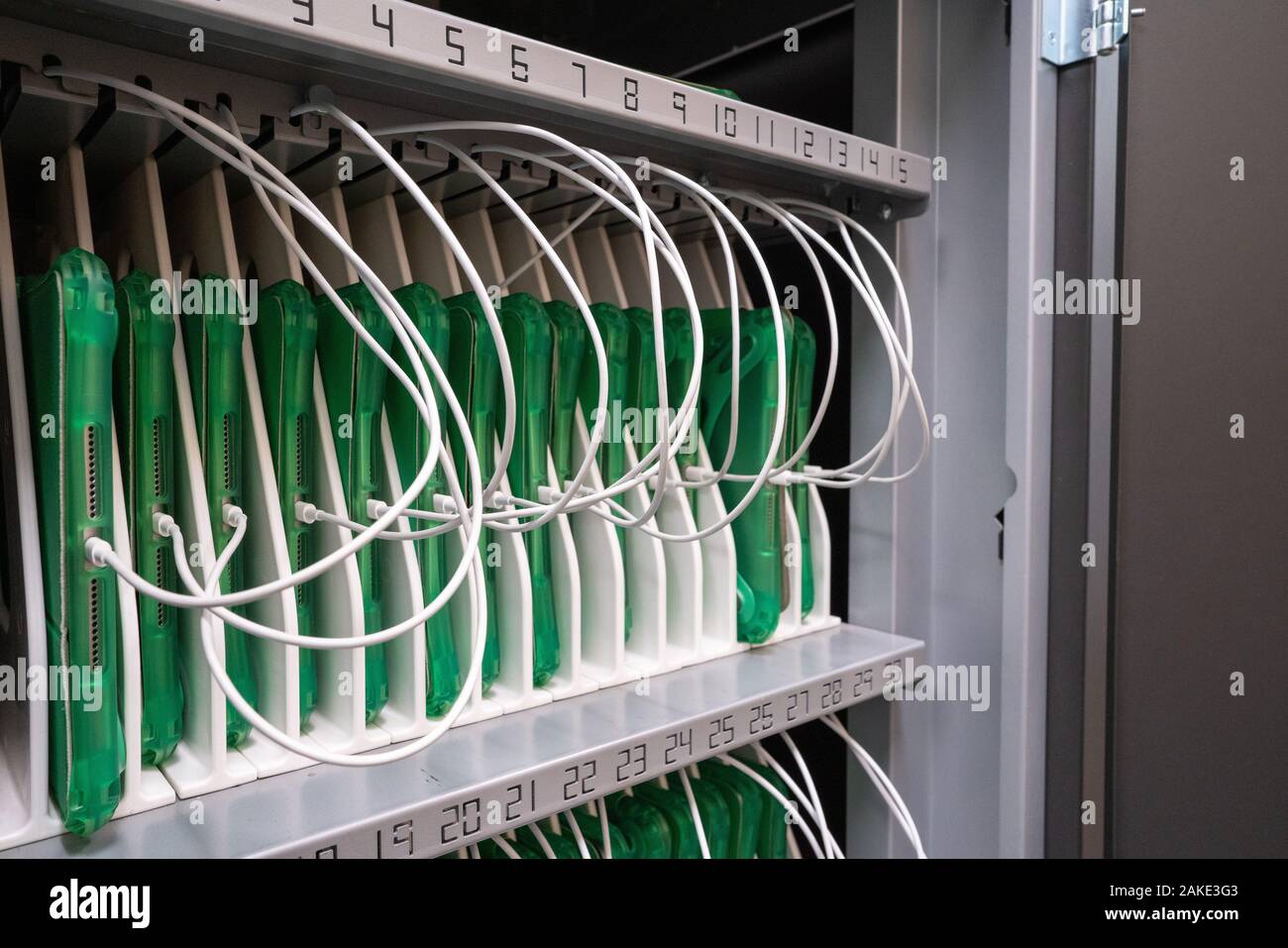 Row of tablets in protective cases being charged in a cabinet in enterprise office location Stock Photo