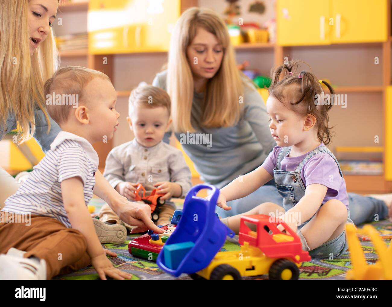Kids toddlers playing in kindergarten or daycare centre under the supervision of moms Stock Photo