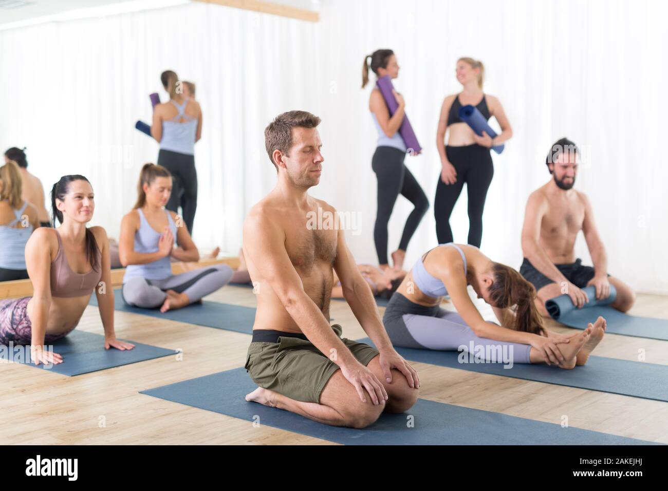 Group of young sporty attractive people in yoga studio, relaxing and socializing after hot yoga class. Healthy active lifestyle, working out in gym. Stock Photo