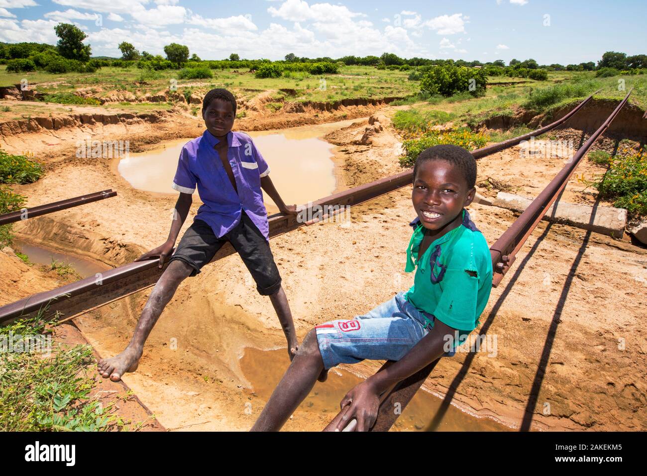 Children playing on tracks of railway bridge swept away by the January 2015 flooding leaving the tracks suspended in mid air, near Bangula. Malawi. March. Stock Photo