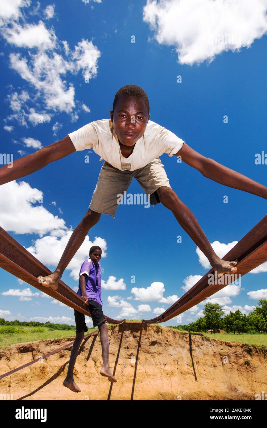 Children playing on tracks of railway bridge swept away by the January 2015 flooding leaving the tracks suspended in mid air, near Bangula. Malawi. March. Stock Photo