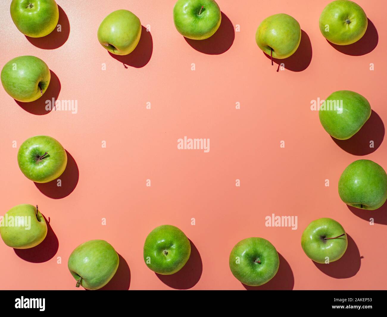 Green apples on orange or coral pink background with copy space for text or design in center, Colorful fruit frame. Flat lay or top view, Hard light Stock Photo