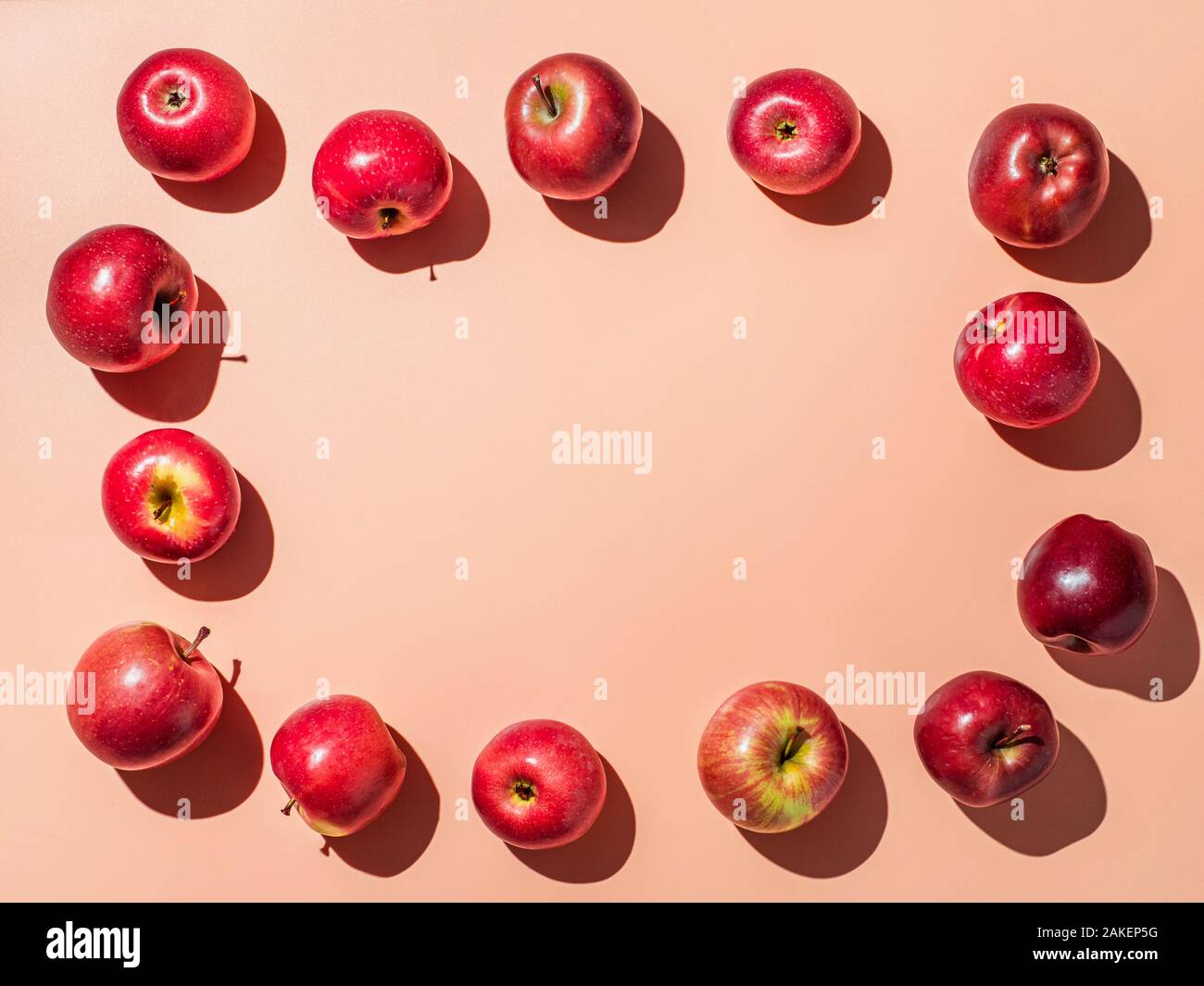 Red apples on orange or coral pink background with copy space for text or design in center, Colorful fruit frame. Creative concept. Flat lay or top view, Hard light Stock Photo