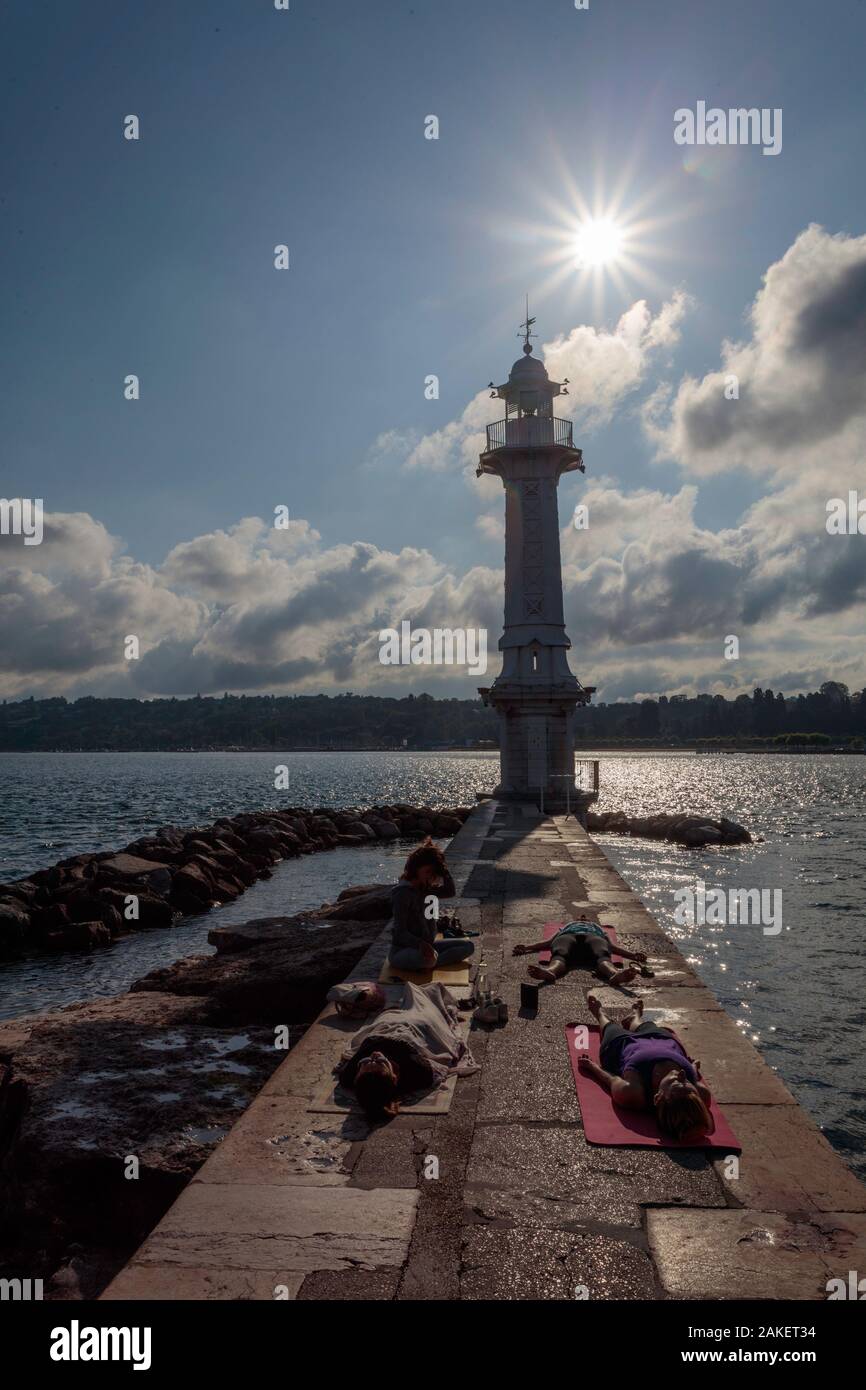 Four people practice yoga and meditation in Bains de Paquis next to the lighthouse. Lake Leman, Geneva. Switzerland Stock Photo