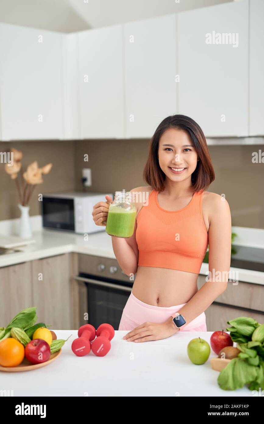 Sportive woman drinking detox juice while standing in the kitchen Stock Photo