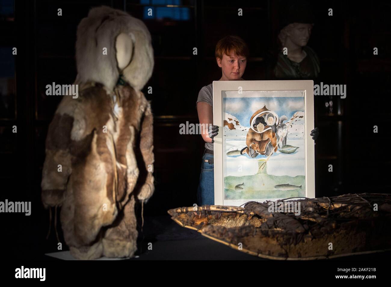 A staff member holds 'There's Another One' by Andrew Qappik 2012, alongside a child's suit made of caribou fur, and a North West Greenlandic Inughuit sled made from narwhal tusk, caribou bone and driftwood, during the preview of the Arctic: Culture and Climate exhibition at the British Museum in London, which will run from May 28 to August 23 2020. Stock Photo