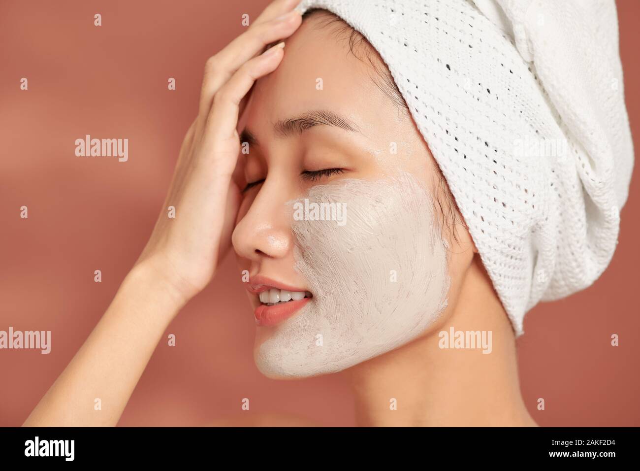 Beautiful cheerful Asian teen girl applying facial clay mask. Beauty treatments, isolated on light background. Stock Photo