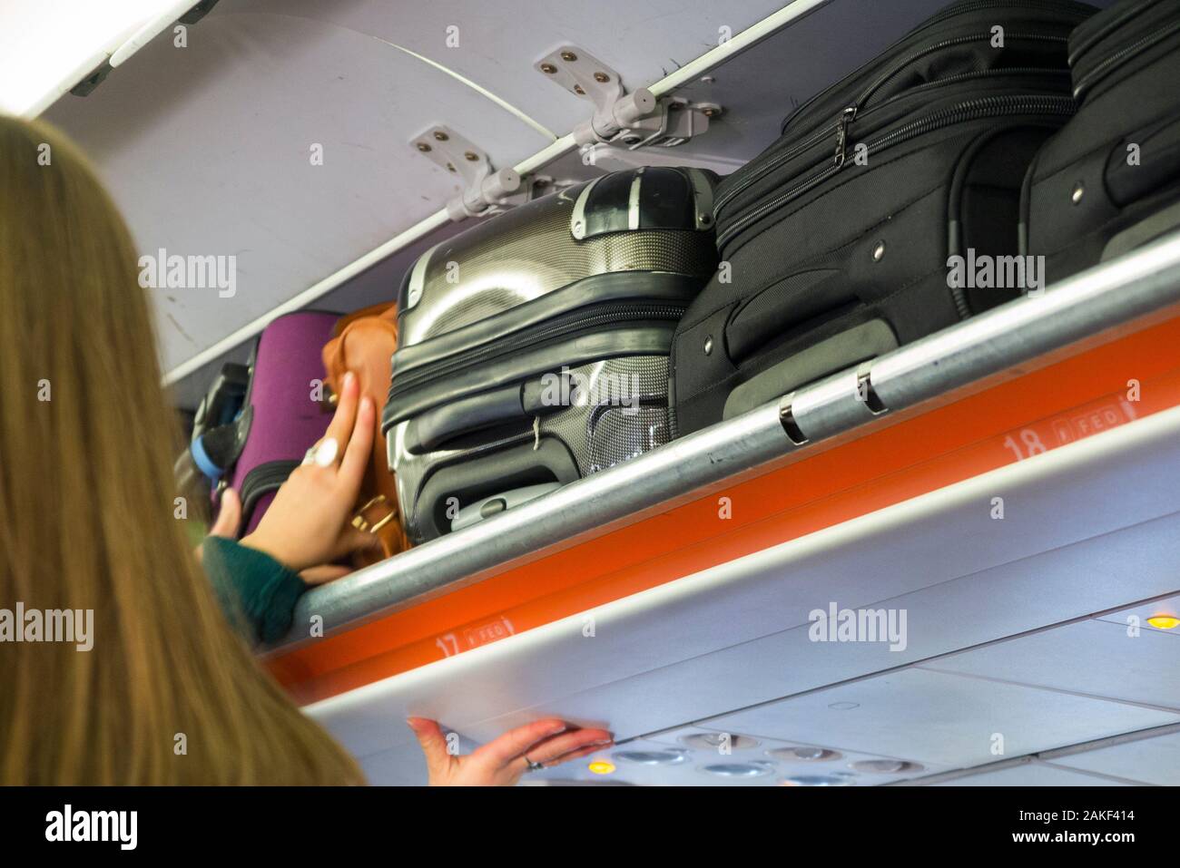 Cabin crew member closing and shutting the overhead passenger locker / lockers / compartment / compartments for stowing passengers bags cabin luggage on an Easyjey Airbus A320 or  A319 plane. (115) Stock Photo