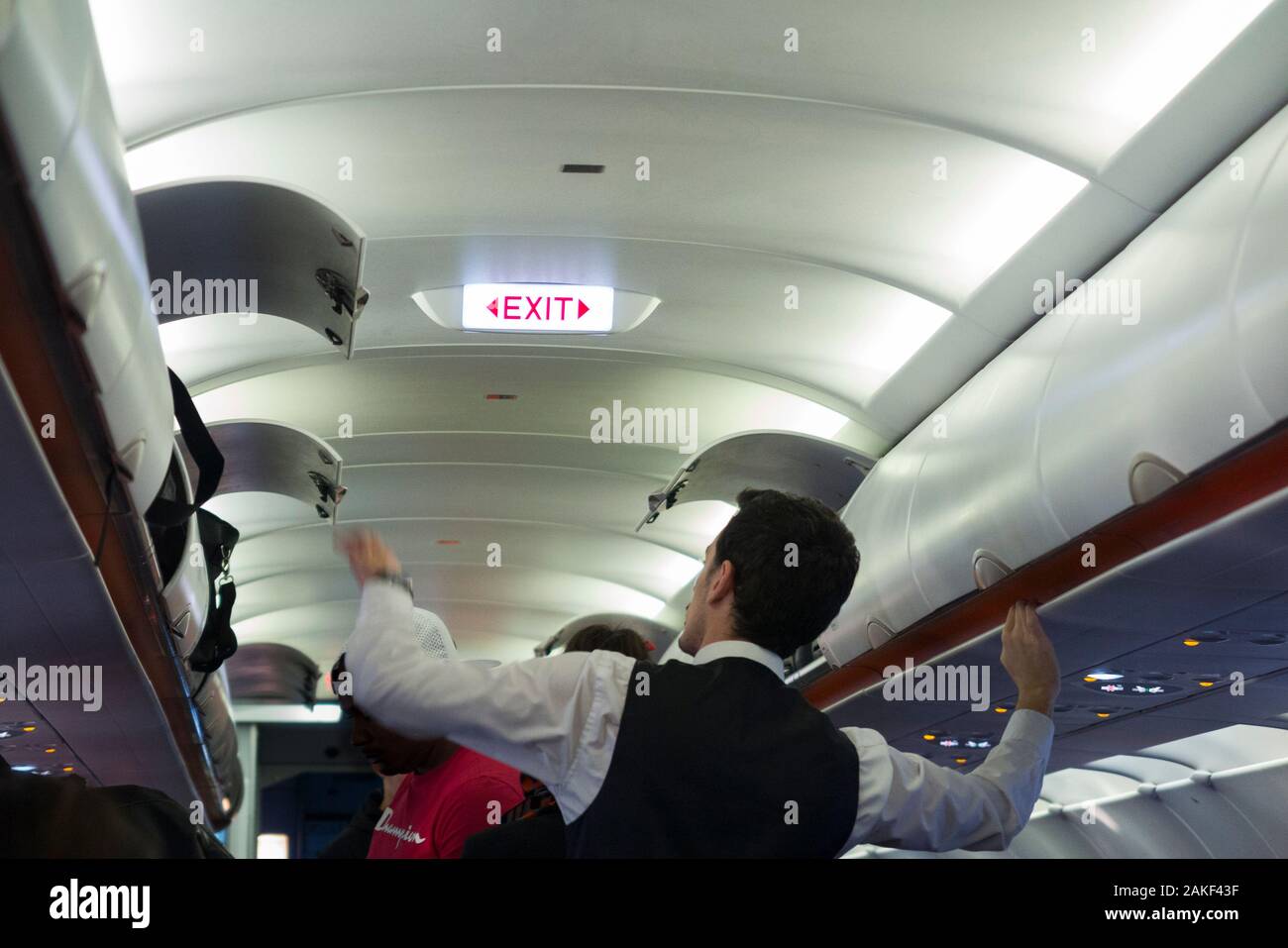 Cabin crew member closing and shutting the overhead passenger locker / lockers / compartment / compartments for stowing passengers bags cabin luggage on an Easyjey Airbus A320 or  A319 plane. (115) Stock Photo