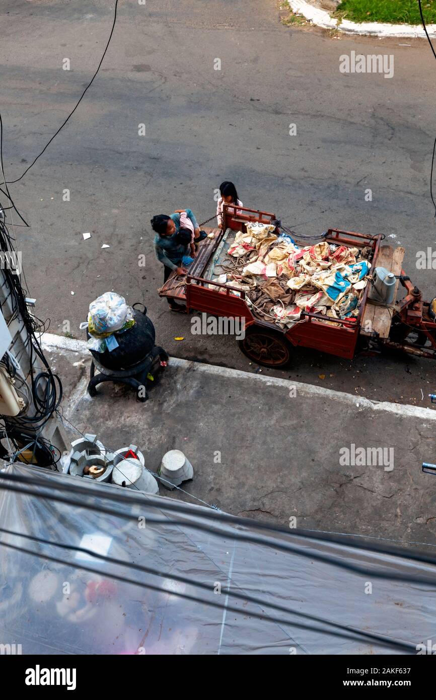A poor homeless scavenger family is gathered around a vehicle used to transport recyclable material on a city street in Kampong Cham, Cambodia. Stock Photo