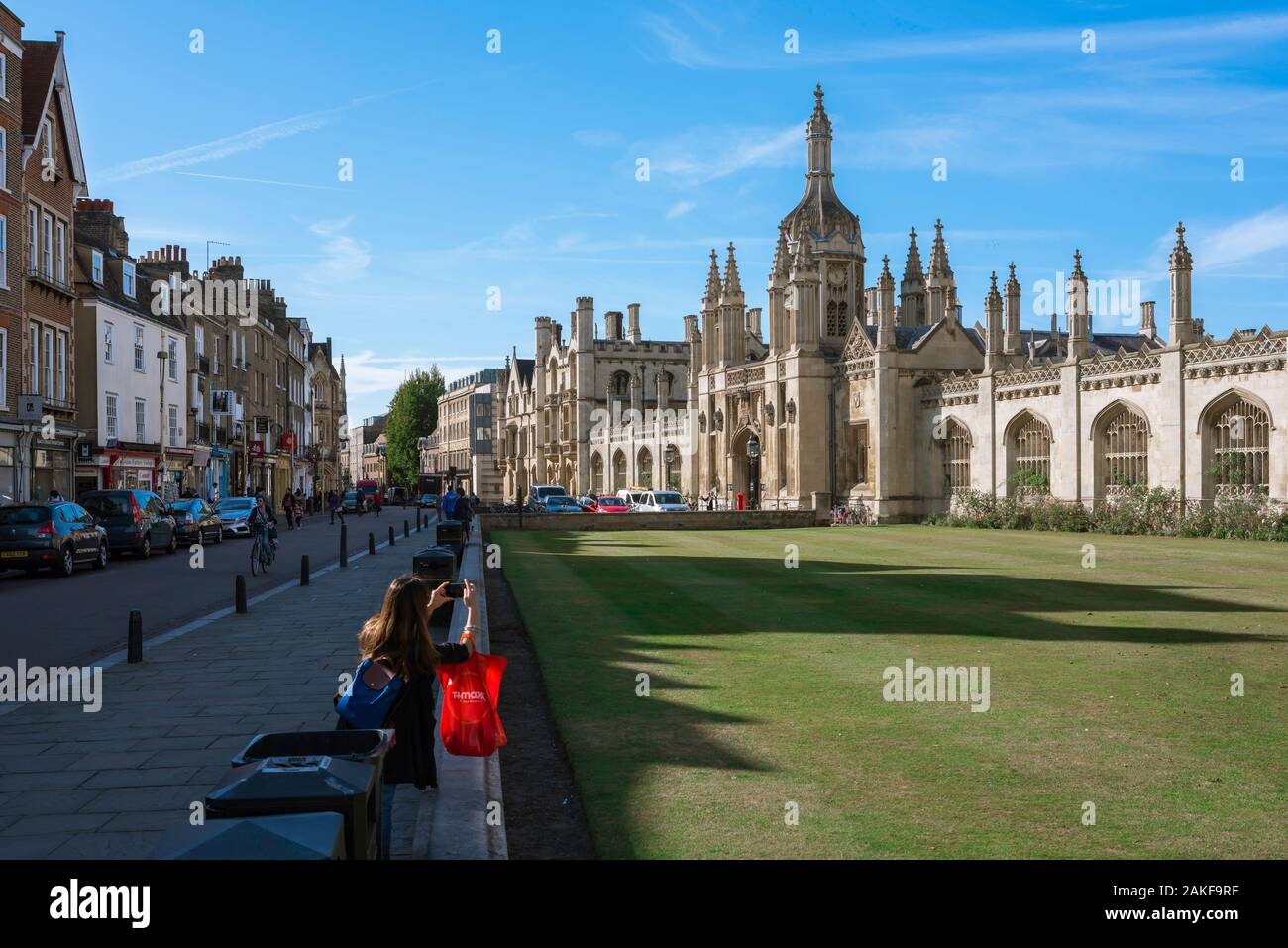 King's Parade Cambridge, rear view of a young woman with a shopping bag taking a photo of the ornate porter's lodge of King's College in Cambridge UK Stock Photo