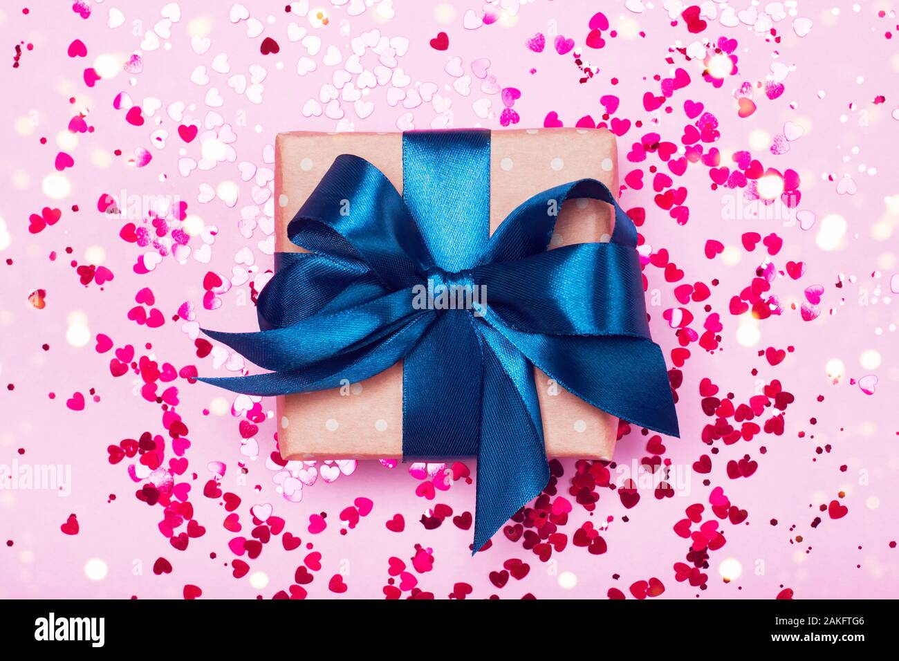 A gift in kraft box with blue bow on a pink background with hearts. Surprise your loved one. The concept of the day of St. Valentine's, birthday and other holidays. Flat lay Stock Photo