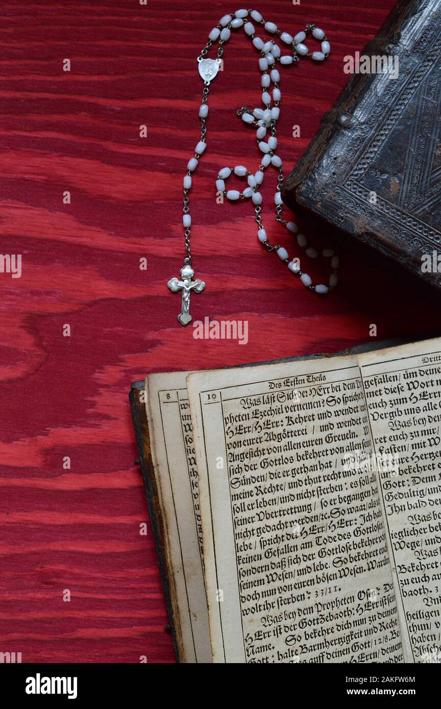 rosary with very old ancient book in old German lettering on red wooden table Stock Photo