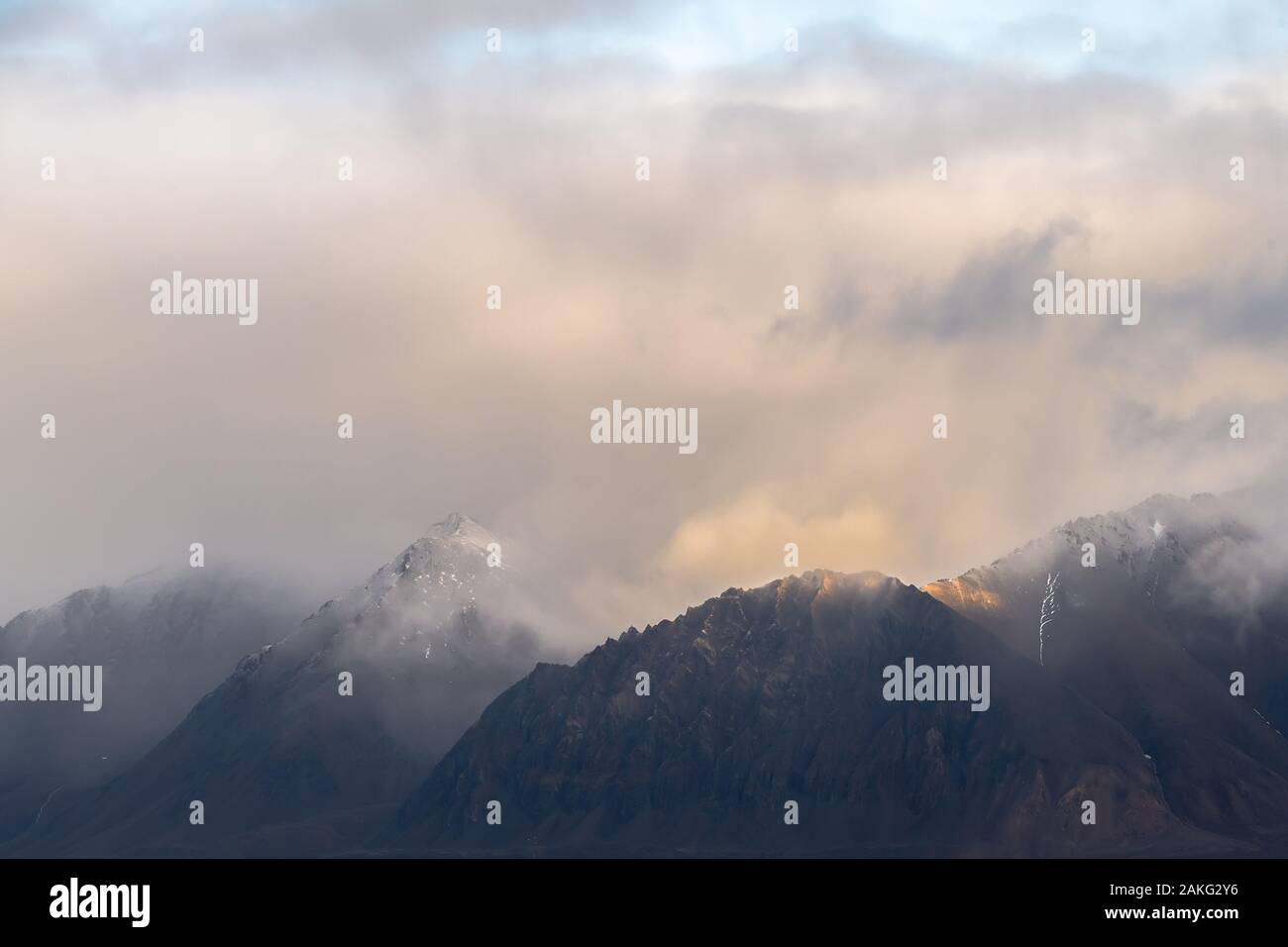 mystically cloudy bright sky over rocky mountain range Stock Photo