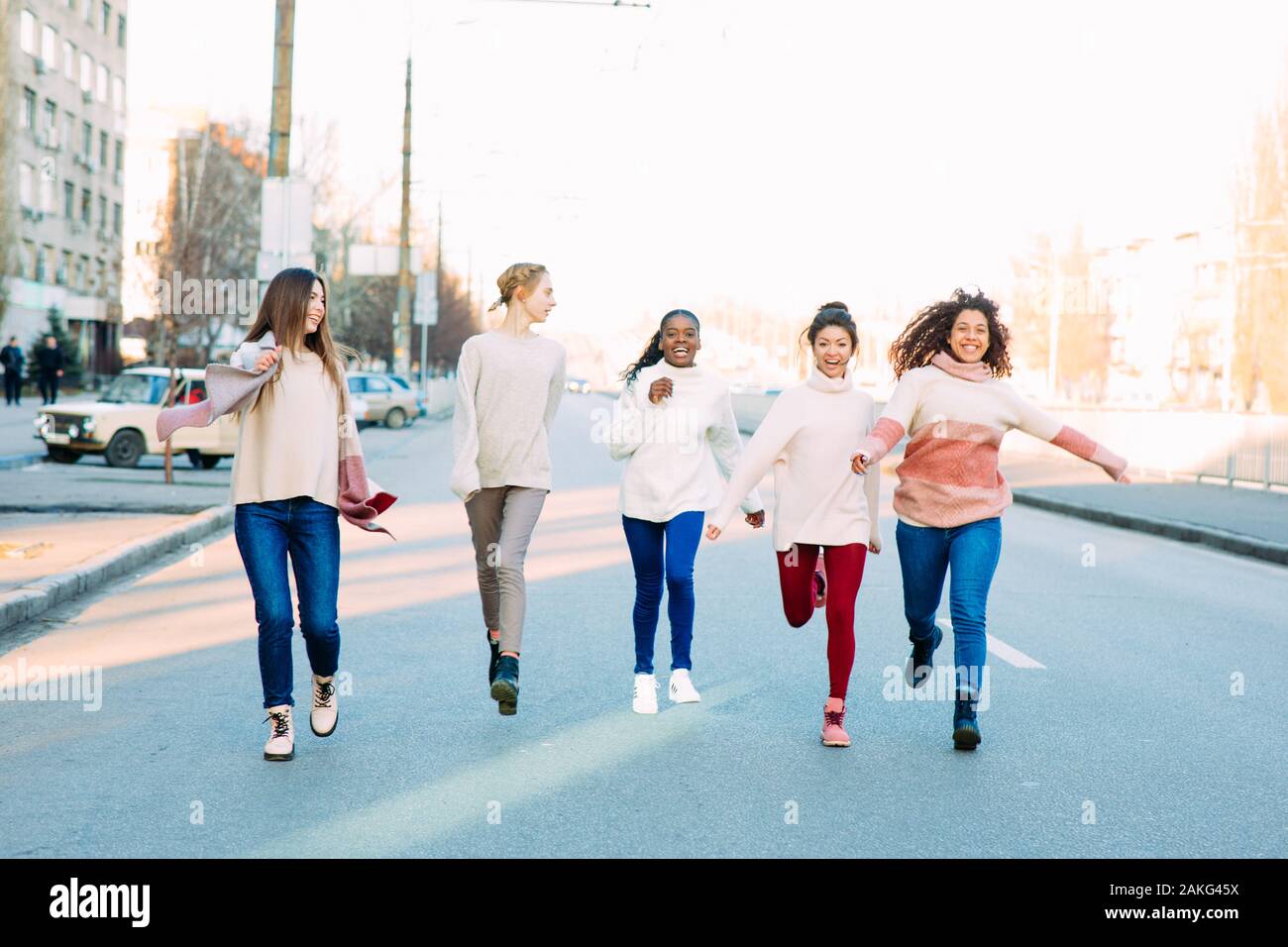 Multiracial group of friends from five young women runs and has a fun on city street. The concept of friendship and unity between different human race Stock Photo