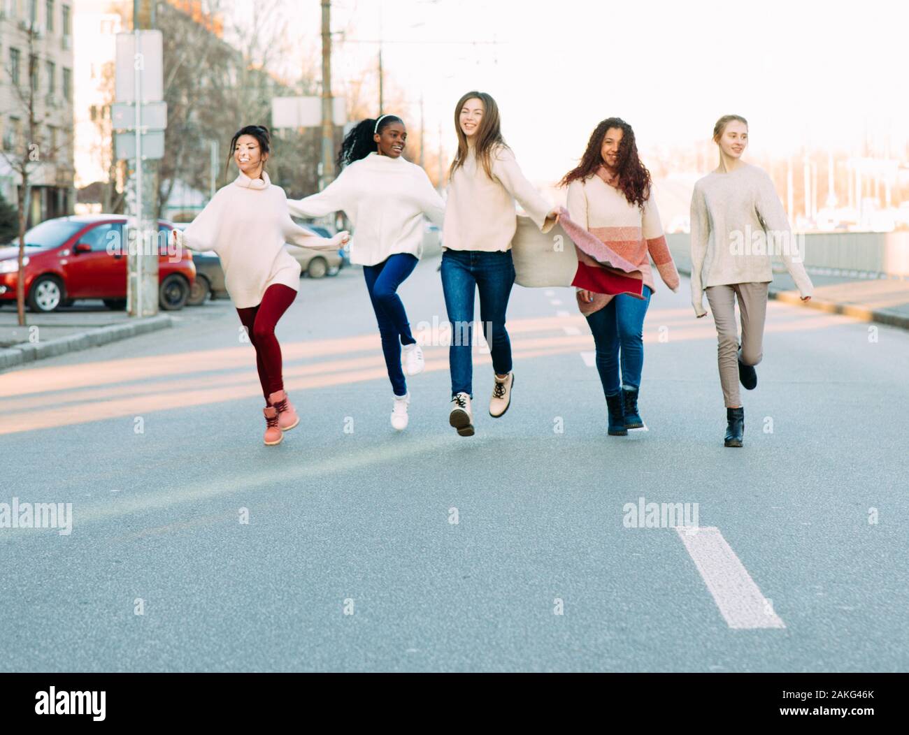 Multiracial group of friends from five young women runs and has a fun on city street. The concept of friendship and unity between different human race Stock Photo