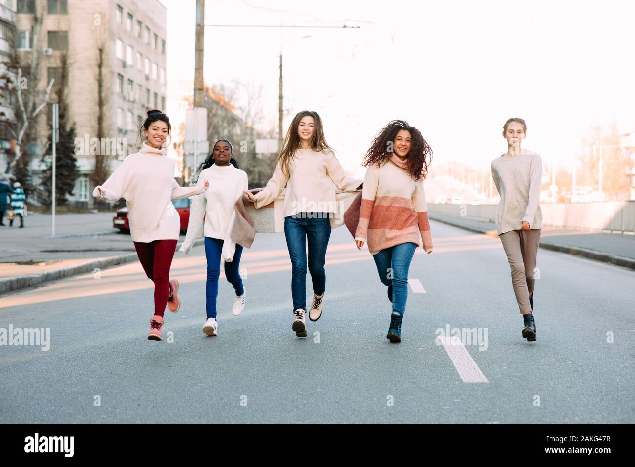 Multiracial group of friends from five young women runs and has a fun on city street. The concept of friendship and unity between different human race Stock Photo