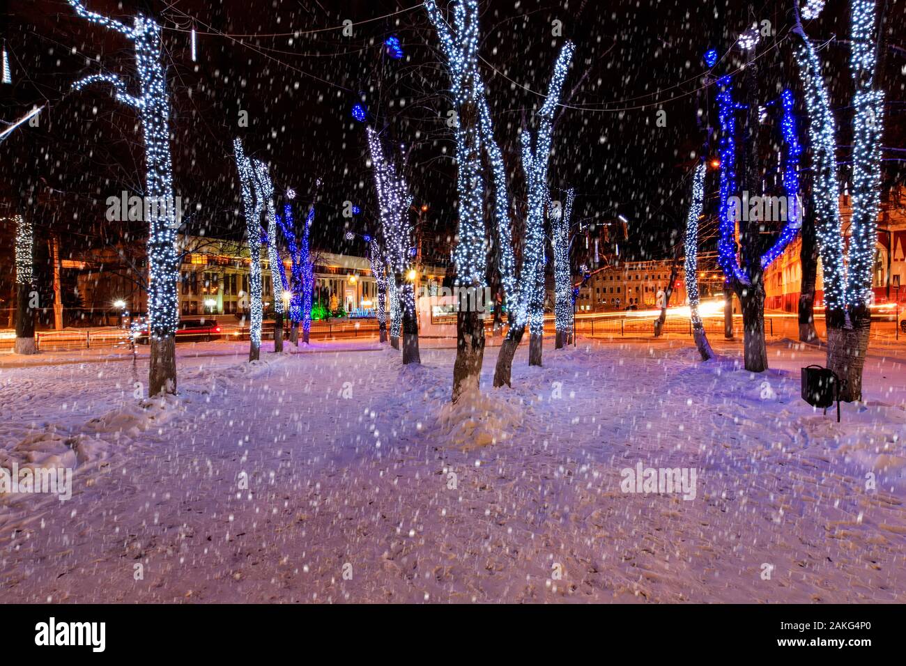 Night park in winter with trees in garlands and falling snow. New Year ...