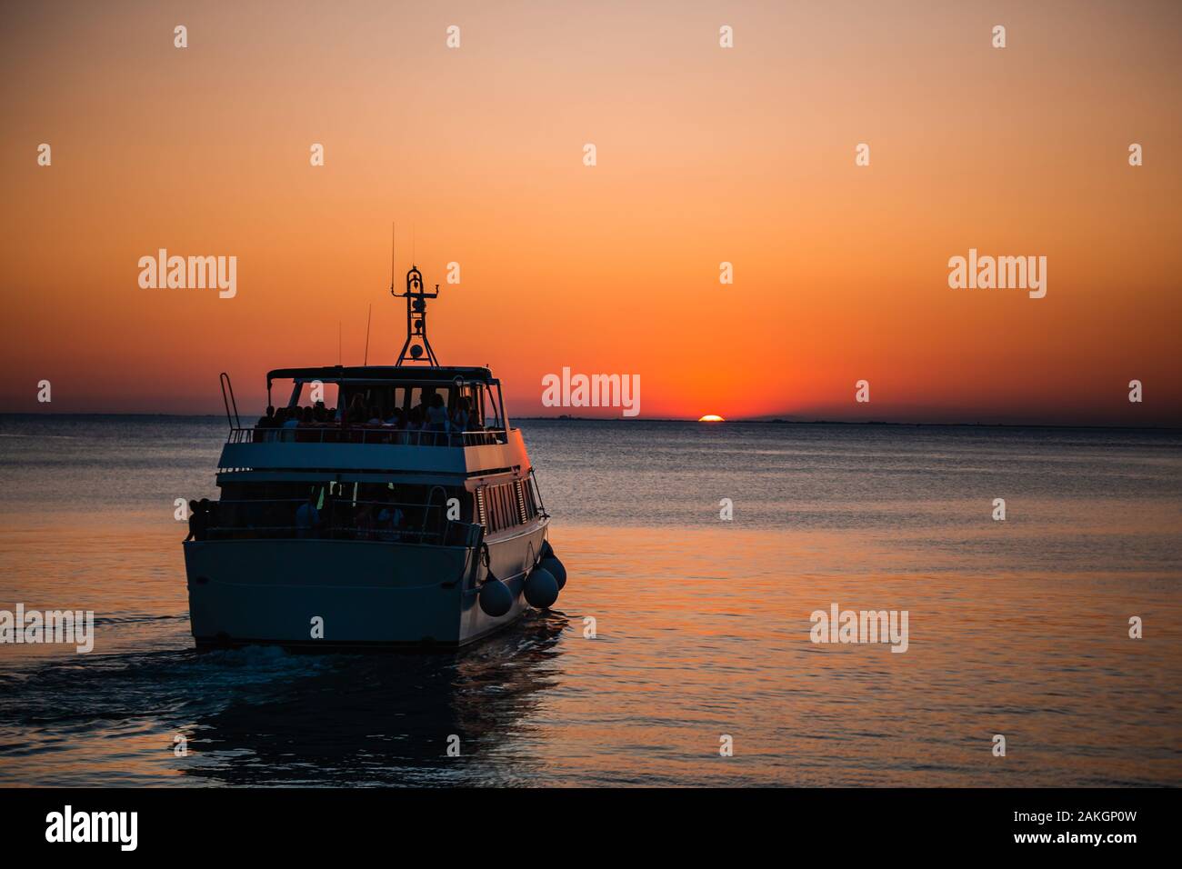 Tourist Boat moving towards the beautiful orange setting sun at dawn in the mediterranean sea in trieste, Italy Stock Photo