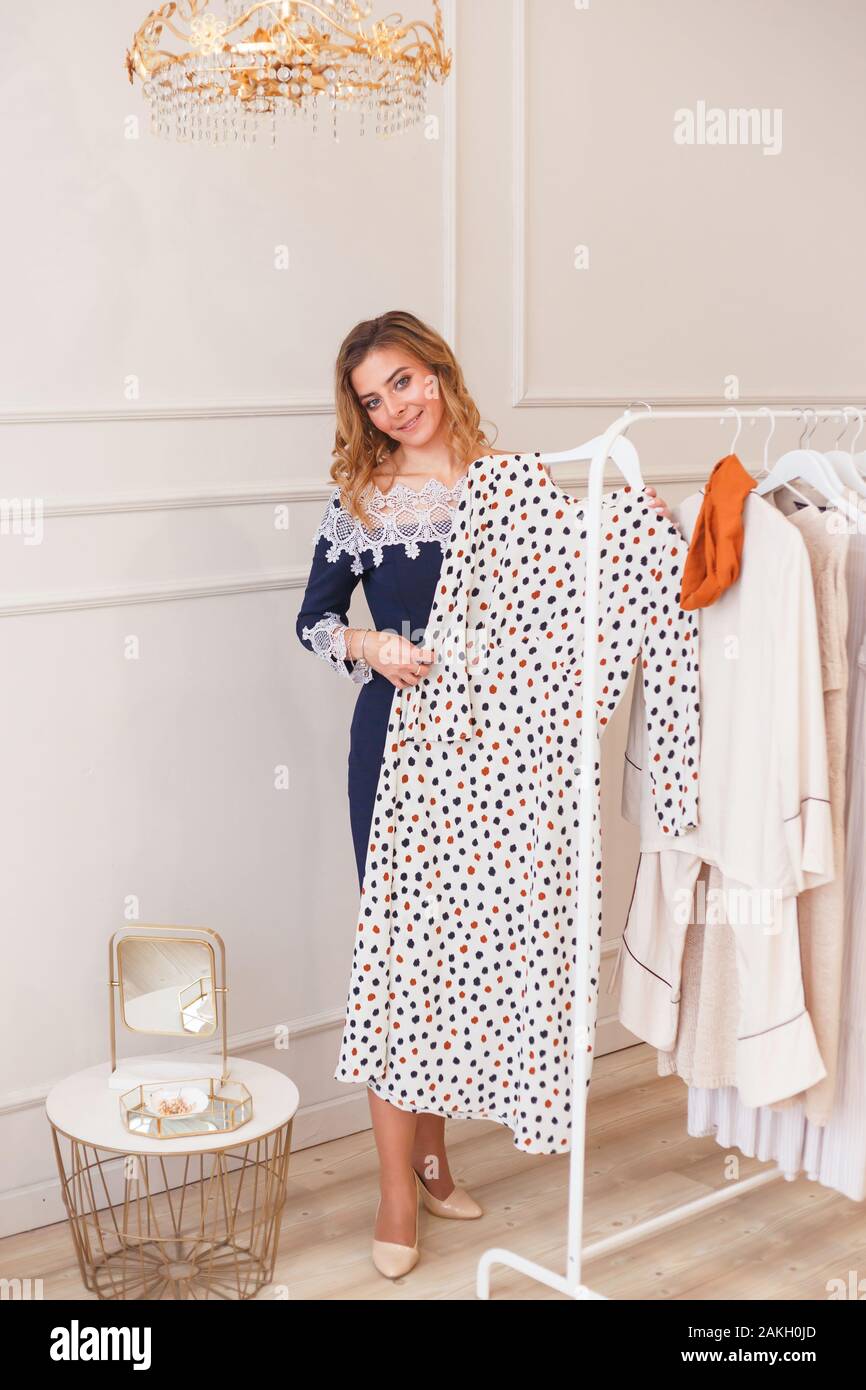 Young woman choosing polka-dot dress among clothes on a rack private showroom Stock Photo