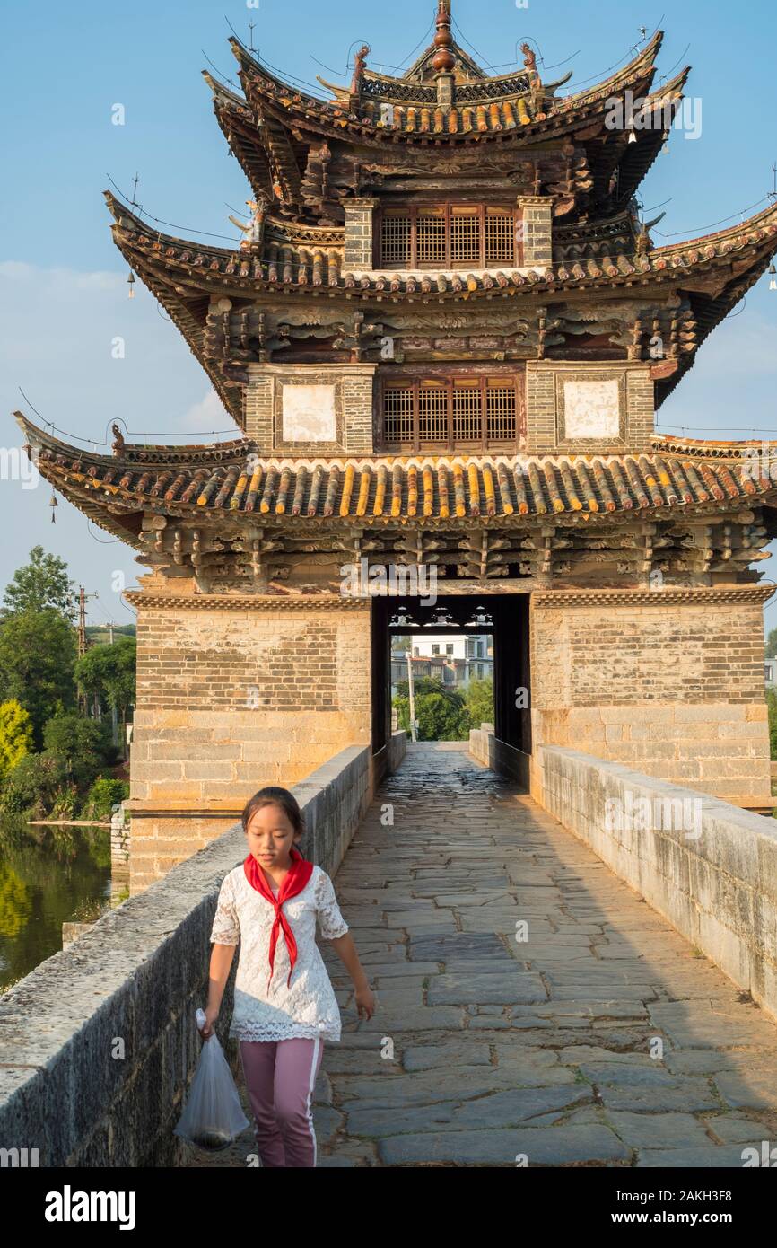 A girl walks in front of the pavilion of the ancient Shuanglong Bridge (Twin Dragon Bridge) in Jianshui, Honghe, Yunnan, China. Stock Photo