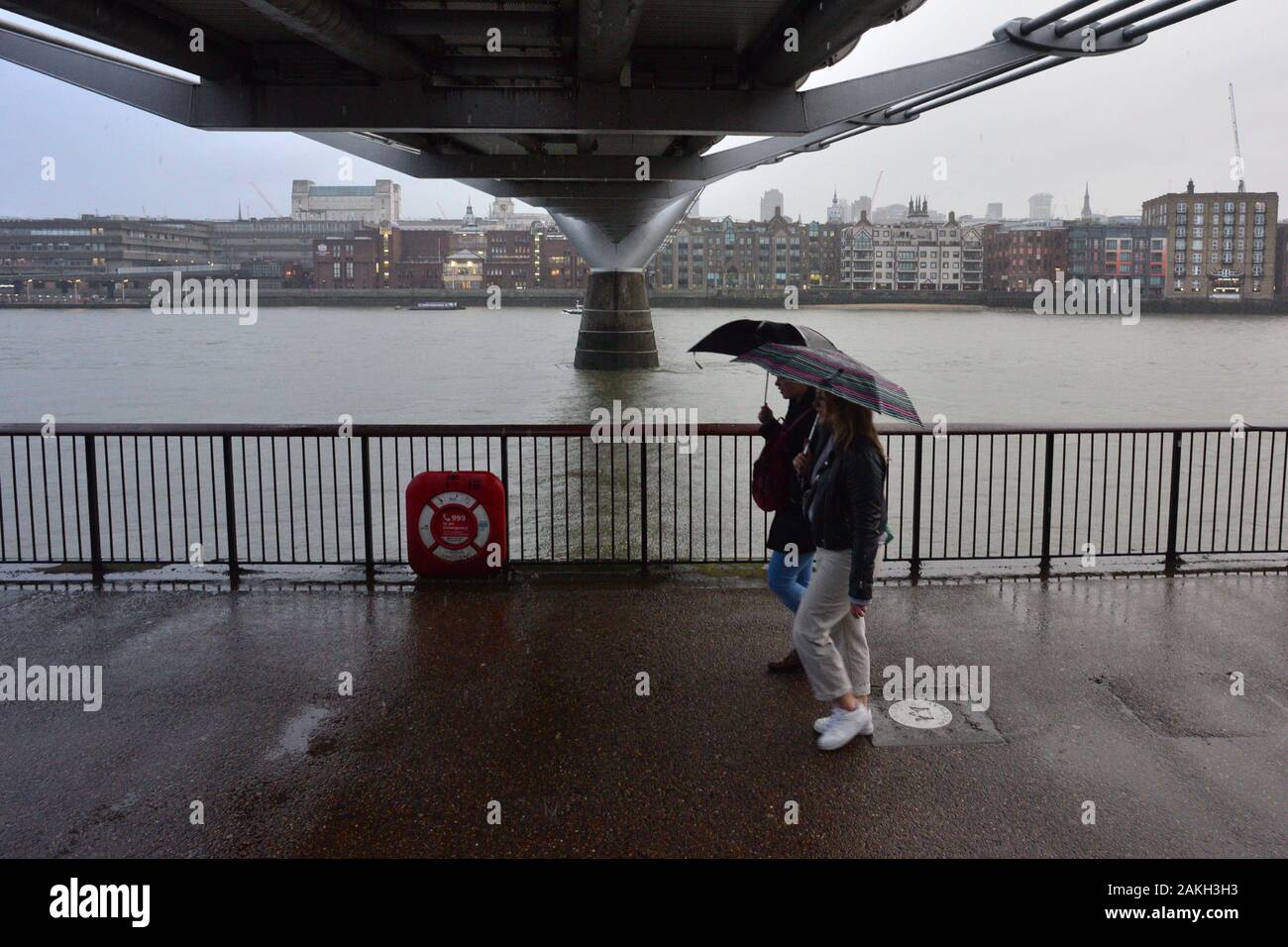 London, UK, 9th January 2020, Weather. Dark afternoon in the city as heavy rain moves in. A couple holding umbrellas walking under Millennium Bridge. Stock Photo