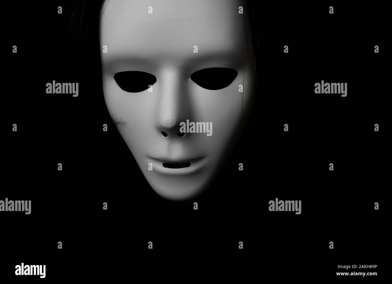 Scary white mask in the dark. Spooky guy in white masquerade. Black, invisible eyes. Black hair. Halloween style. Stock Photo