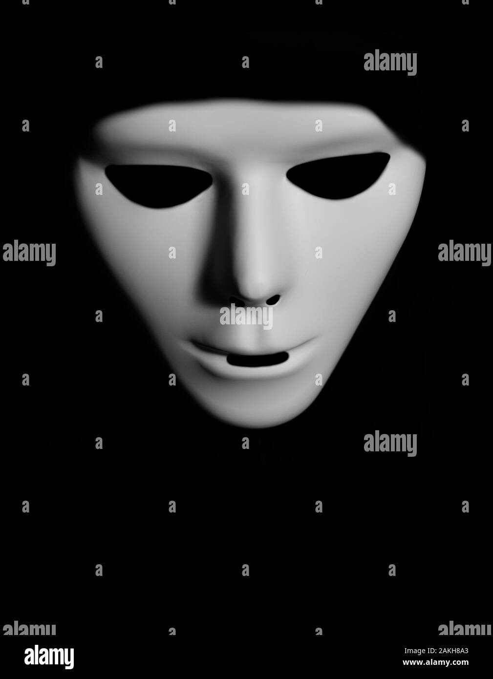 Scary white mask in the dark. Spooky guy in white masquerade. Black, invisible eyes. Black hood. Halloween style. Stock Photo