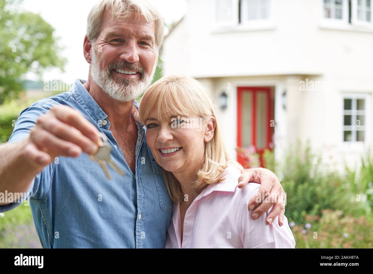Portrait Of Mature Couple Standing In Garden In Front Of Dream Home In Countryside Holding Keysmature Stock Photo