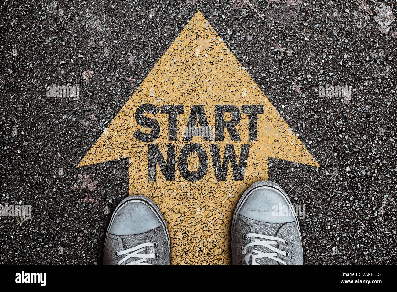 high angle view of person standing on arrow marking on asphalt, road with text START NOW, motivation concept Stock Photo