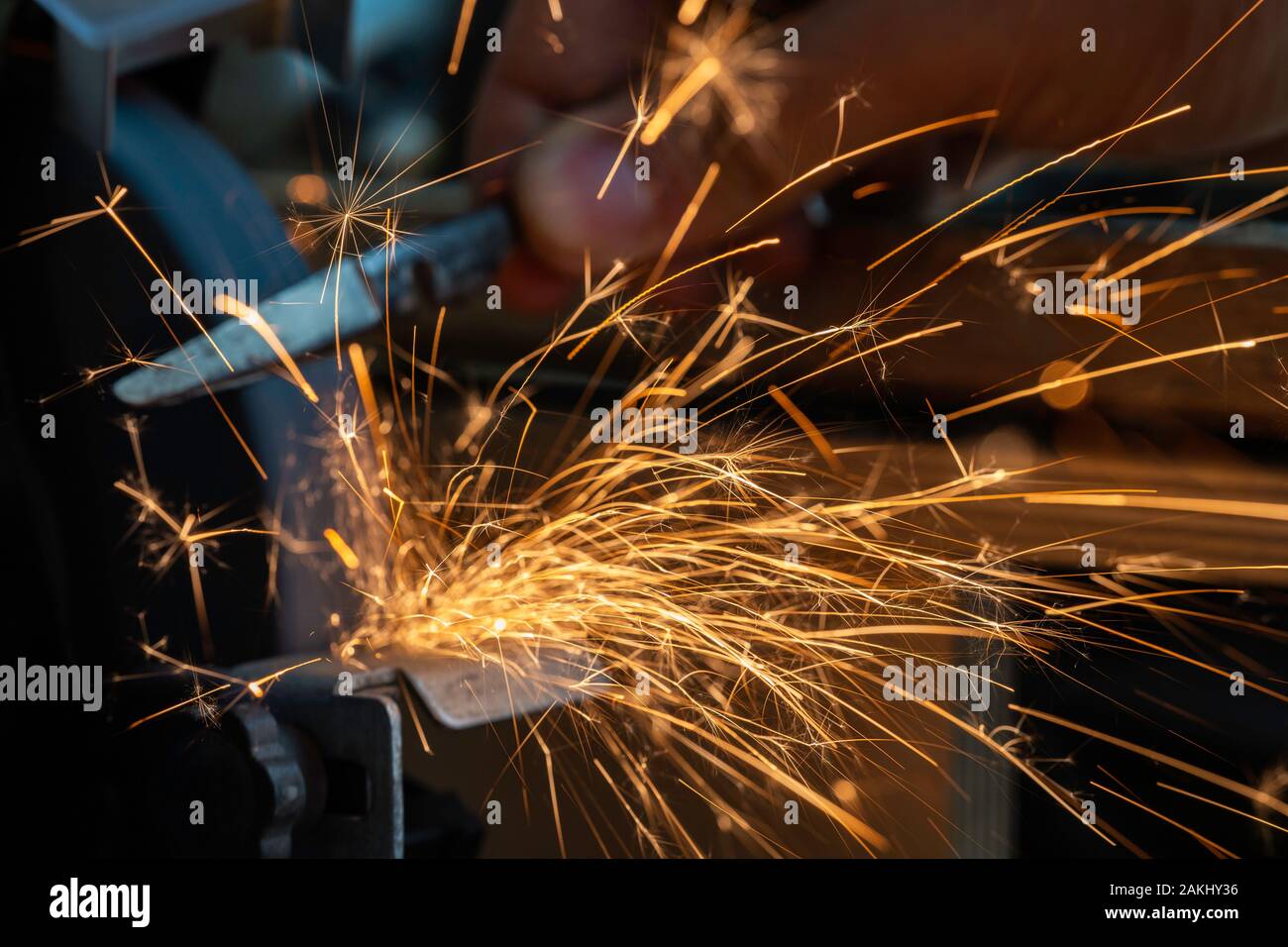 Sparks fly out of the grinder during use. A knife is sharpened on the grinder. Stock Photo