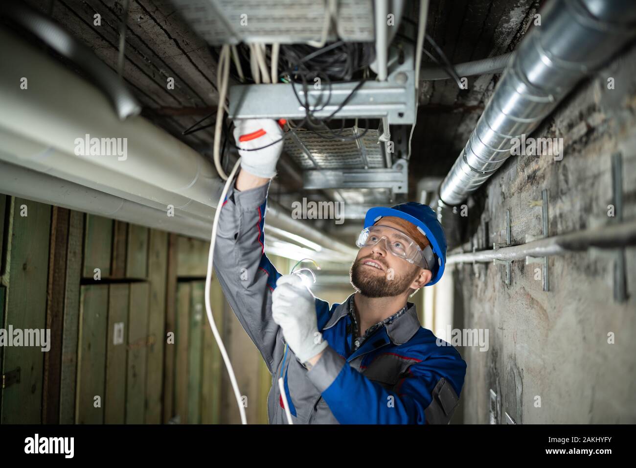 Male Worker Wearing Hard Hat Connecting Cables Stock Photo