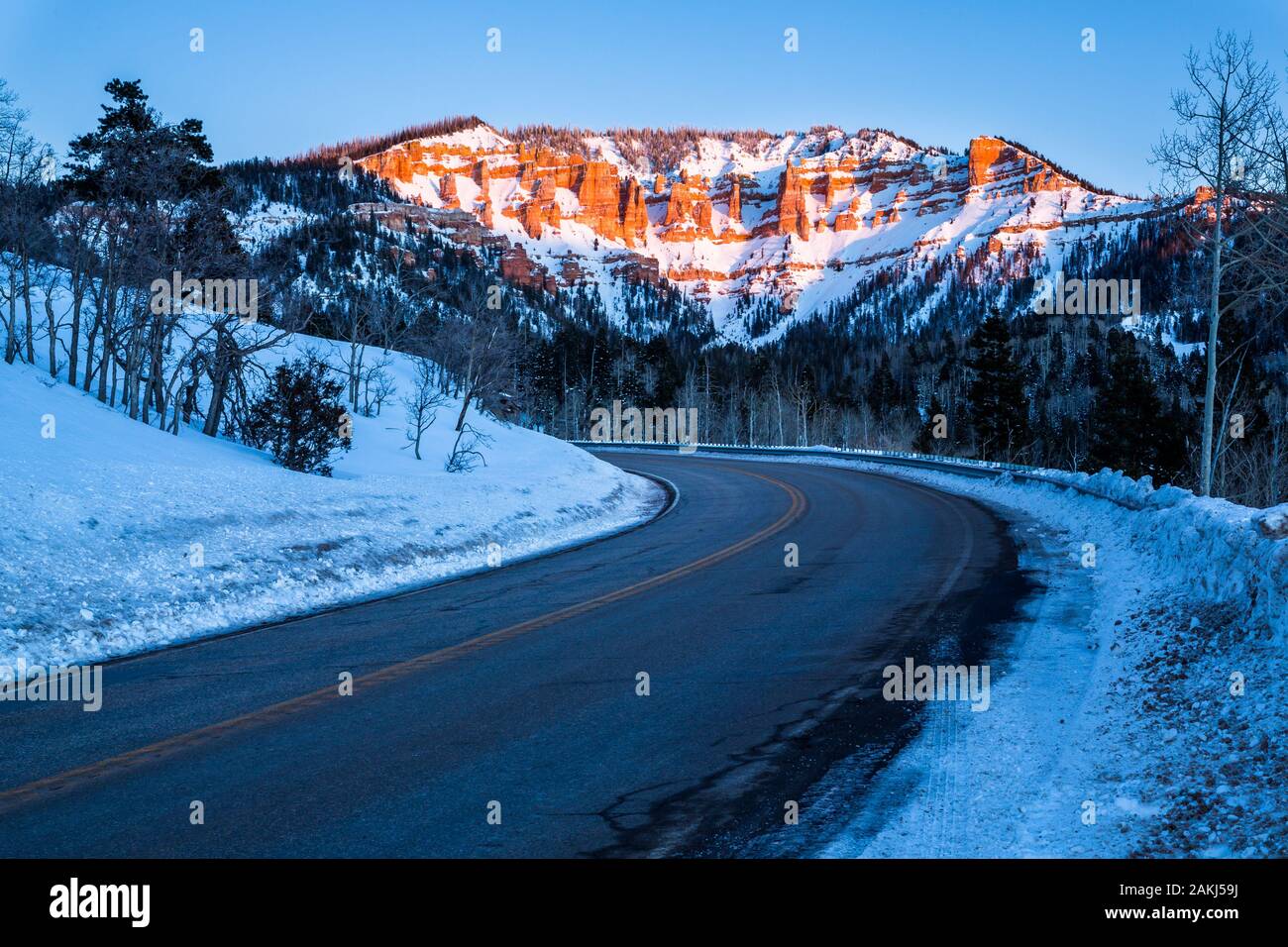Road traveling toward desert sandstone formations near Bryce Canyon and Cedar Breaks in Southern Utah desert. Snow covers the ground and pink light of Stock Photo
