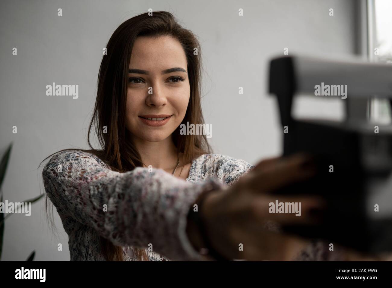 Smiling young brunette woman takes photographs selfie portrait with old photo camera. Stock Photo