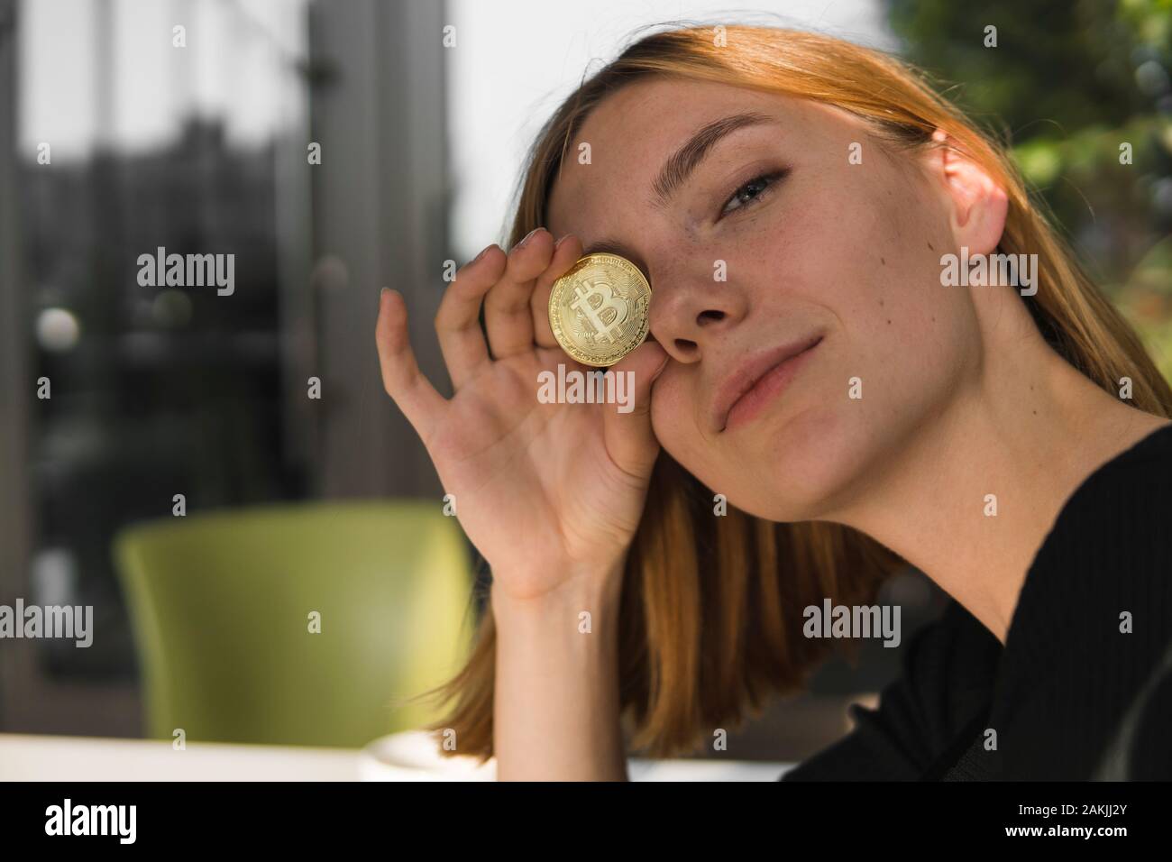 A nice girl is attaching a gold coin to her eye. Bitcoins, crypto currency,  electronic money. Woman sitting in cafe holding bitcoin in front eye Stock  Photo - Alamy