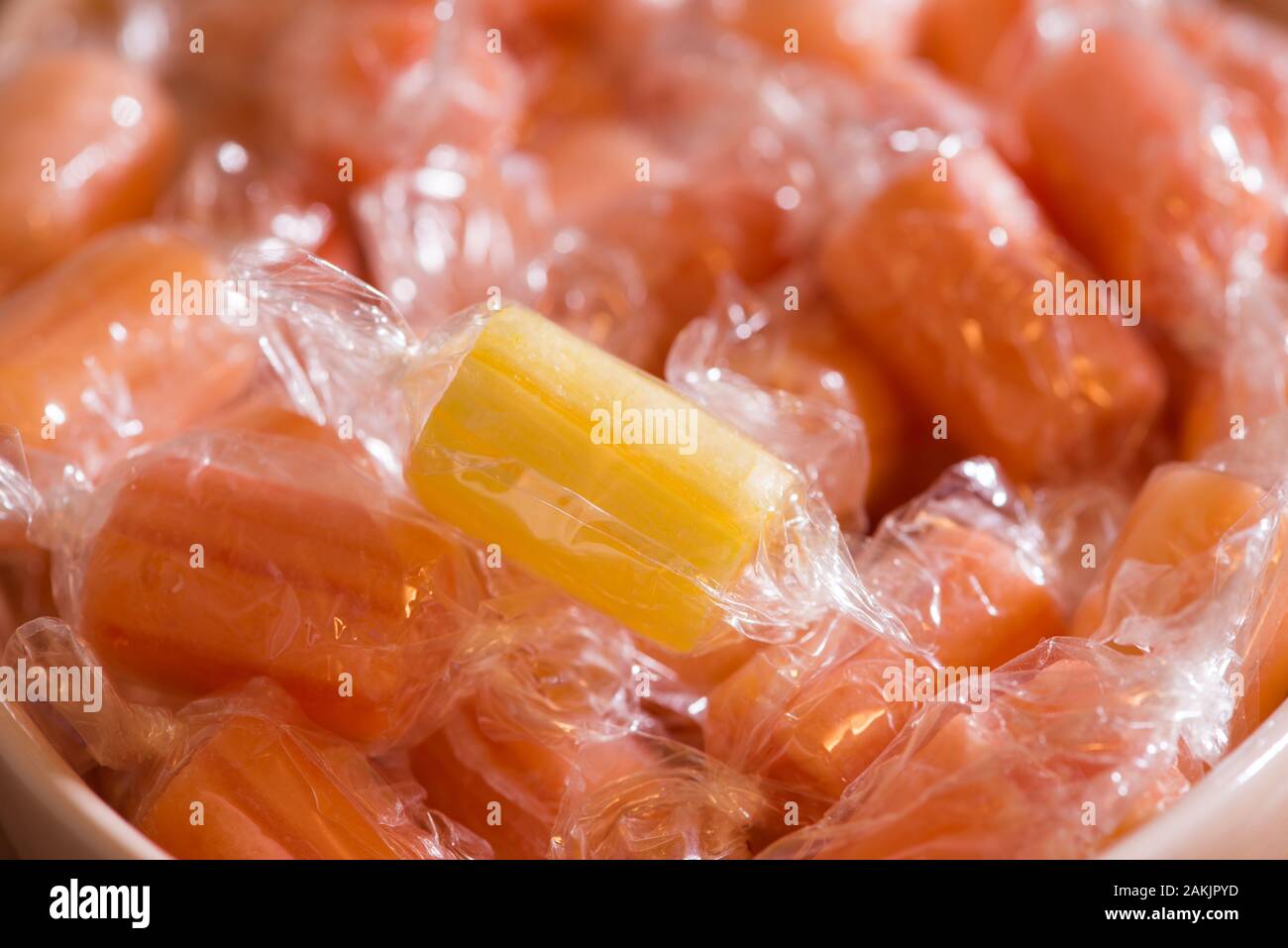 A single yellow hard boiled sweet sits on a plate of red sweets Stock Photo