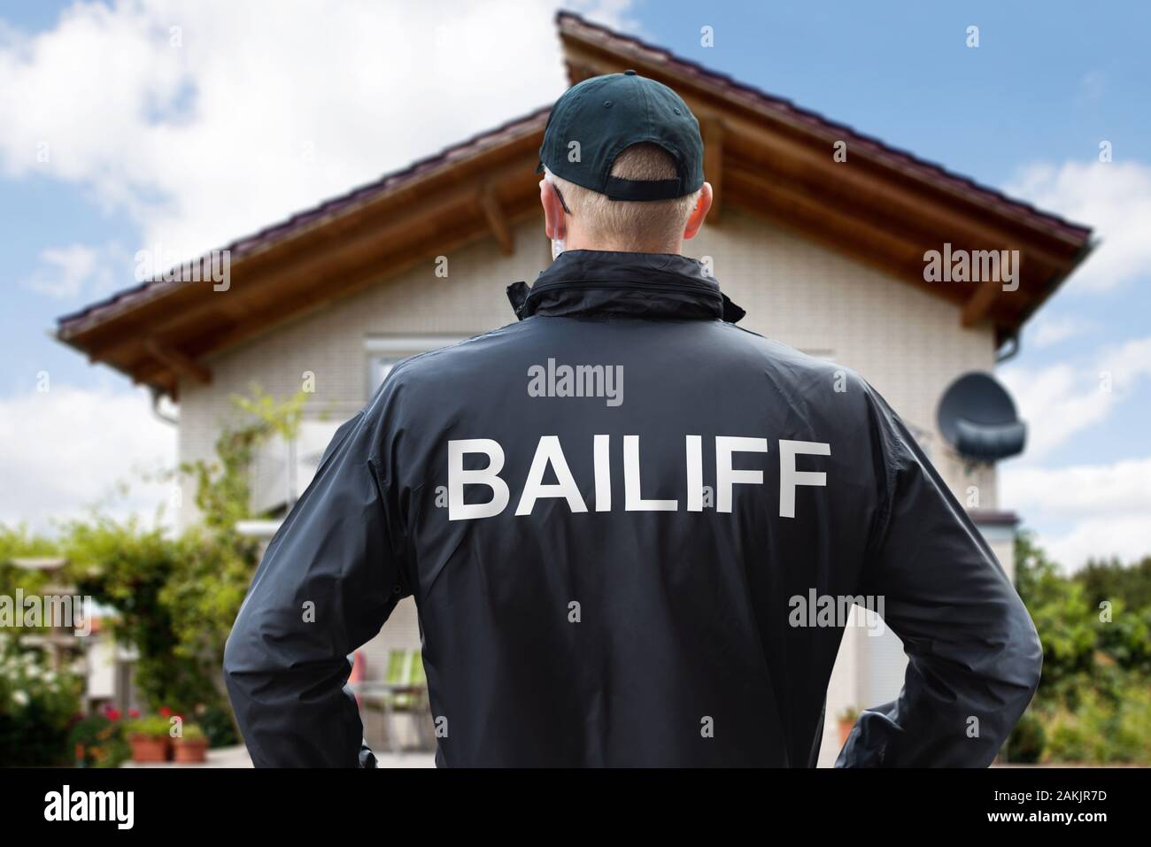 Rear View Of A Male Bailiff Standing With His Hands On Hips At House Rear View Of A Male Bailiff Standing With His Hands On Hips At House