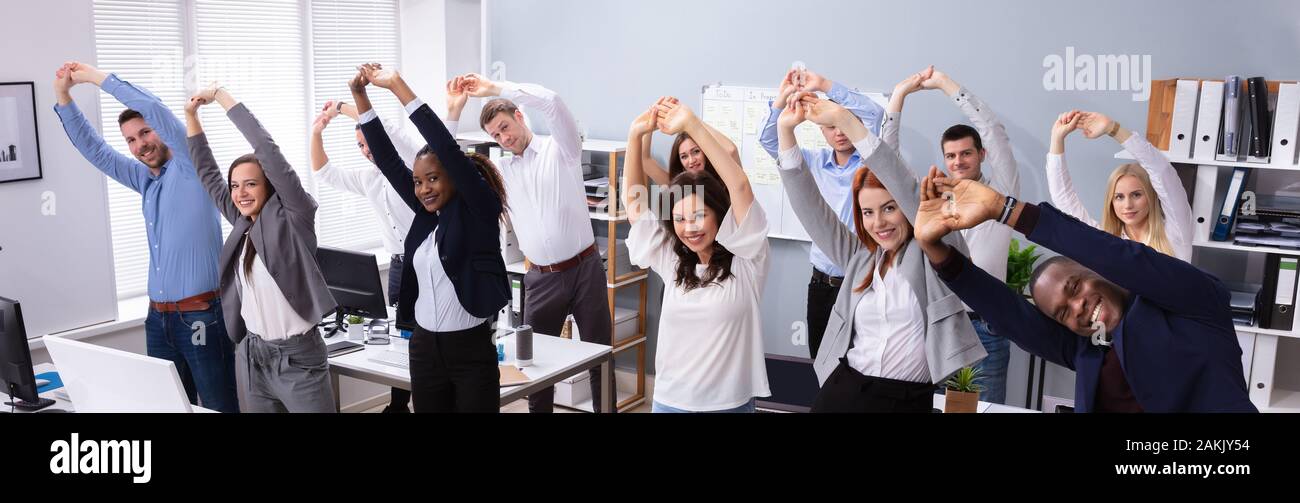 Group Of Smiling Multi-ethnic Young Office Workers Doing Stretching Exercise At Workplace Stock Photo