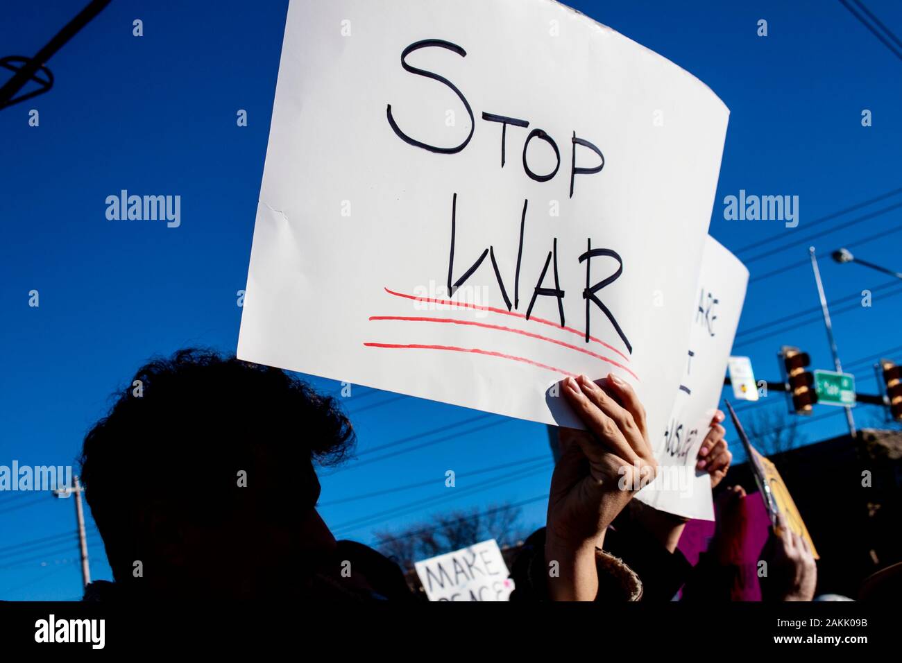 War protestor - Man on street corner holding up Stop War sign with other protestors in distance Stock Photo