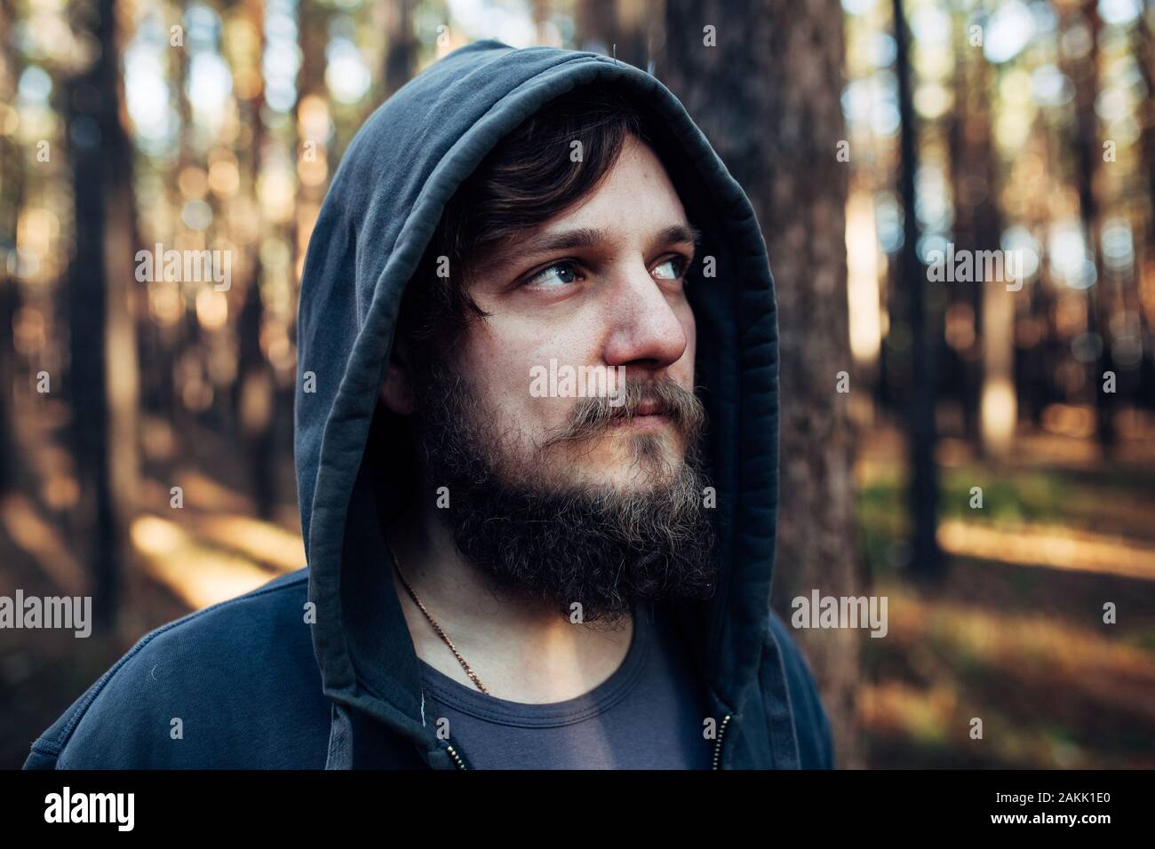 Man is standing in the forest and just relaxing dressed like homeless in dark blue goodie downshifting concept Stock Photo