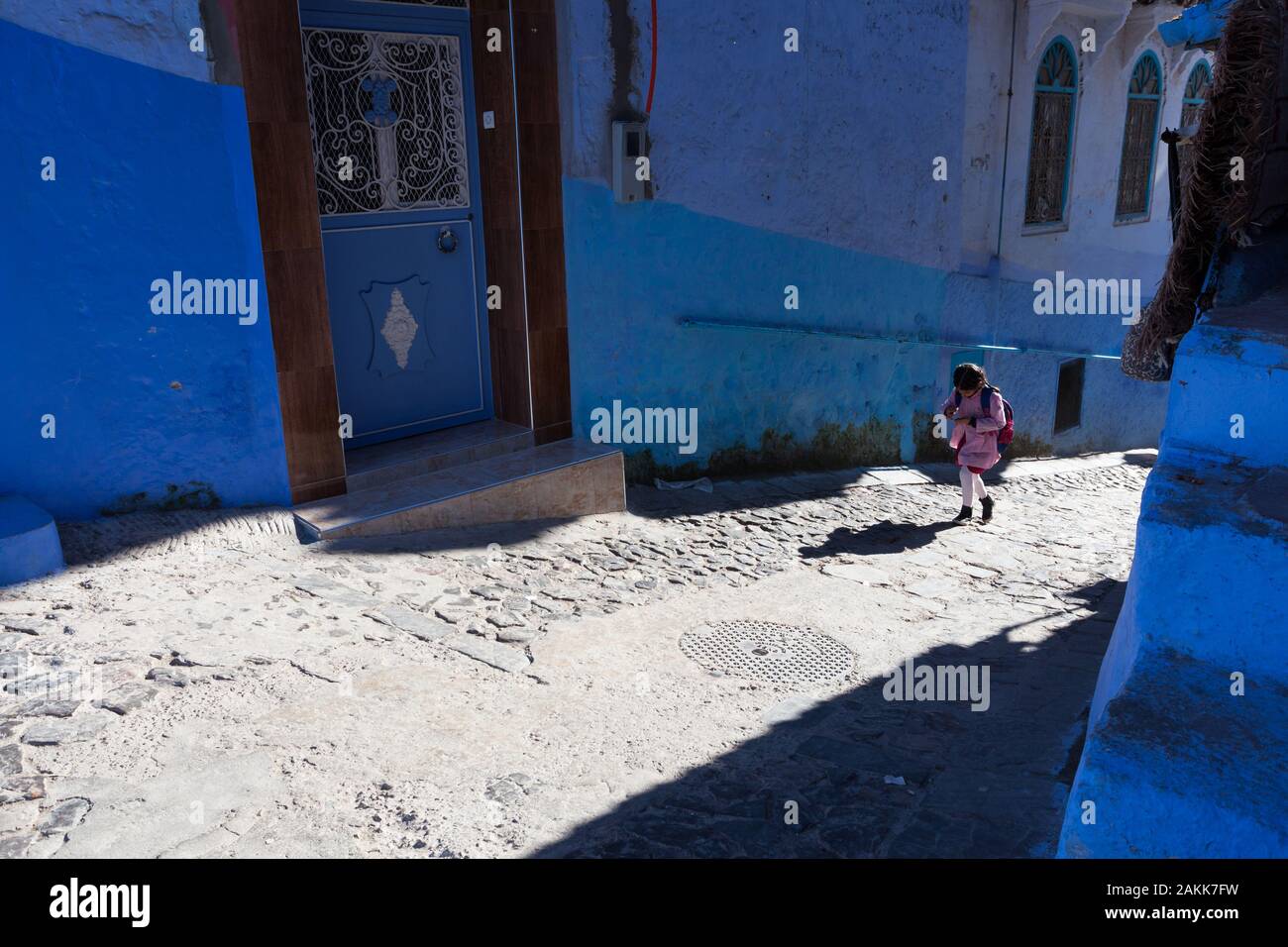 Young girl with schoolbag in the sunlit street of medina of Chefchaouen (also known as Chaouen), Morocco Stock Photo