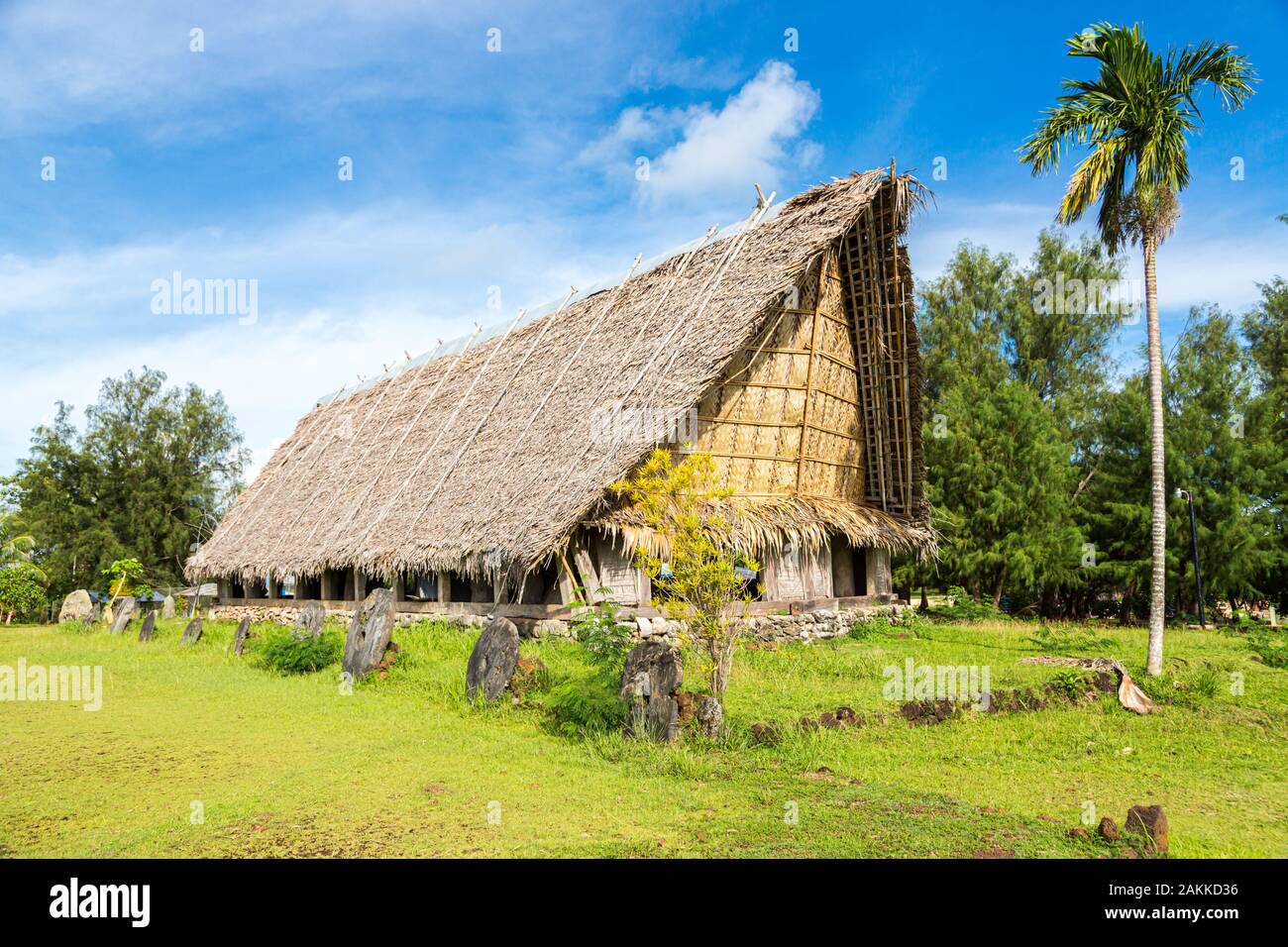 Traditional thatched yapese men's meeting house called faluw or fale and a bank of historic megalithic stone money rai in front of it. A high coconut Stock Photo